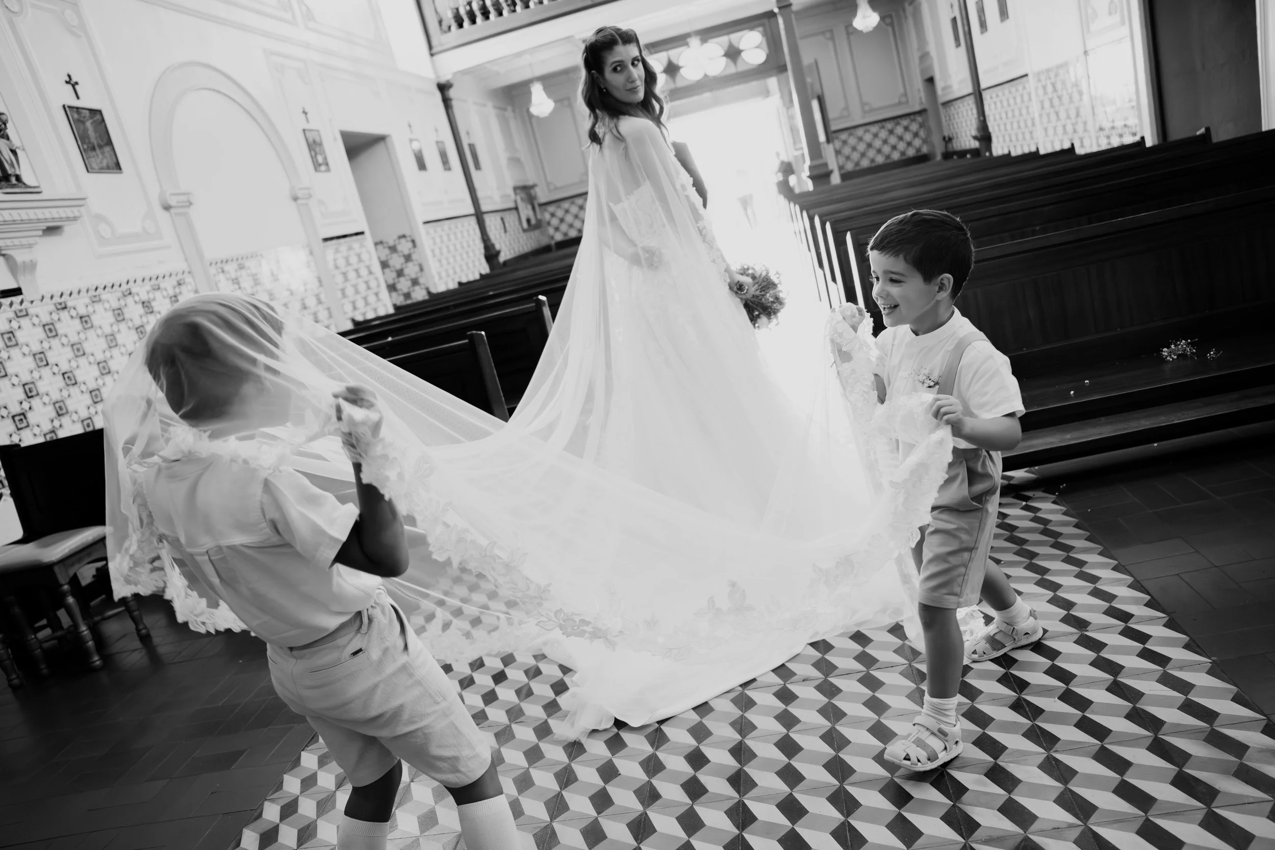 Bride walking inside a church with children holding her dress during a wedding ceremony in Portugal