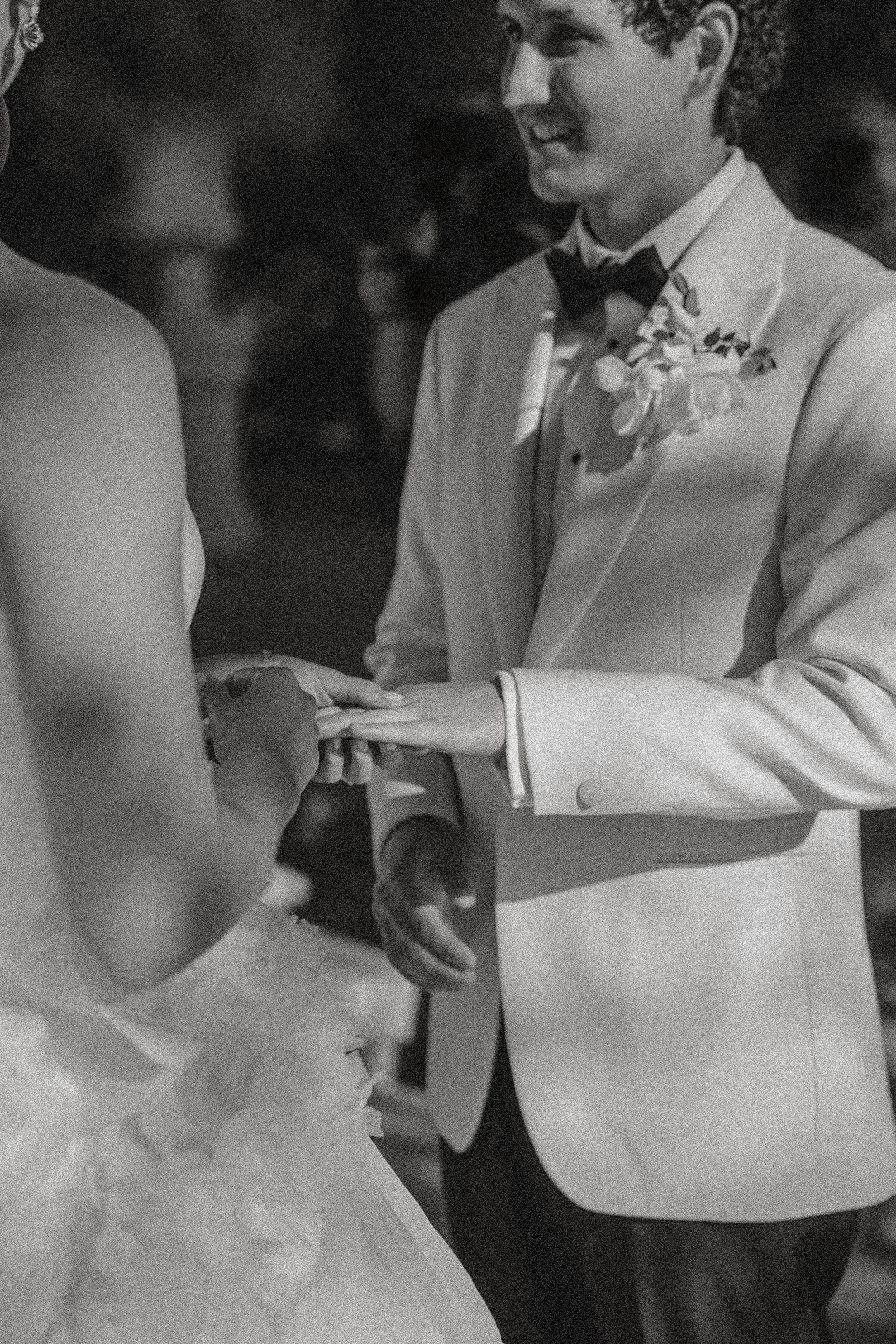 A groom in a tuxedo with a boutonniere exchanges wedding vows with a bride wearing a wedding dress.