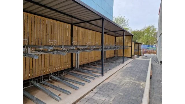Bike racks underneath a metal canopy outside a building with wooden fence panels.