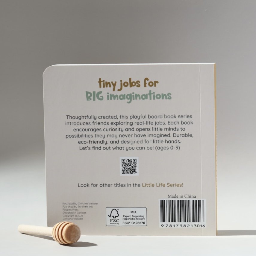 Back of a children's board book titled "Tiny Jobs for Big Imaginings" with a wooden honey dipper placed in front. The book introduces exploration of real-life jobs through a playful series for ages 0-3, made in China, and contains a QR code.