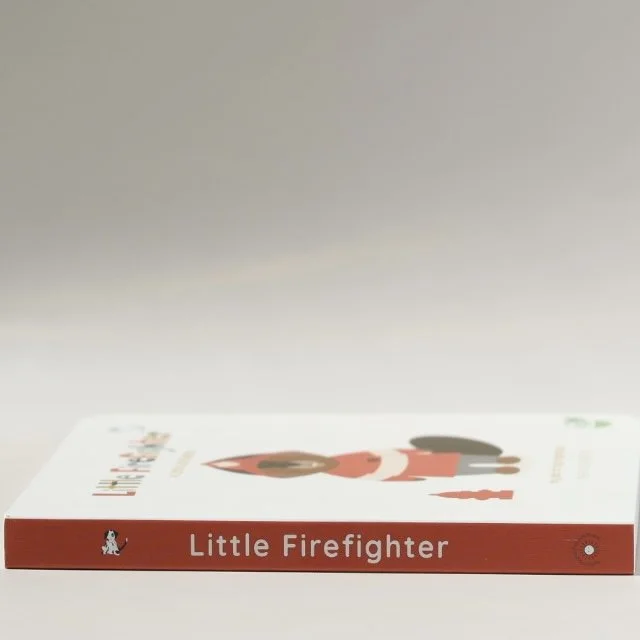 A children's book titled 'Little Firefighter' with an illustration of a girl firefighter on the cover, lying flat on a plain white surface.