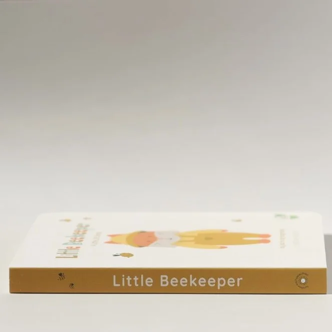 A children's book titled "Little Beekeeper" lies flat on a white surface with the cover facing up.