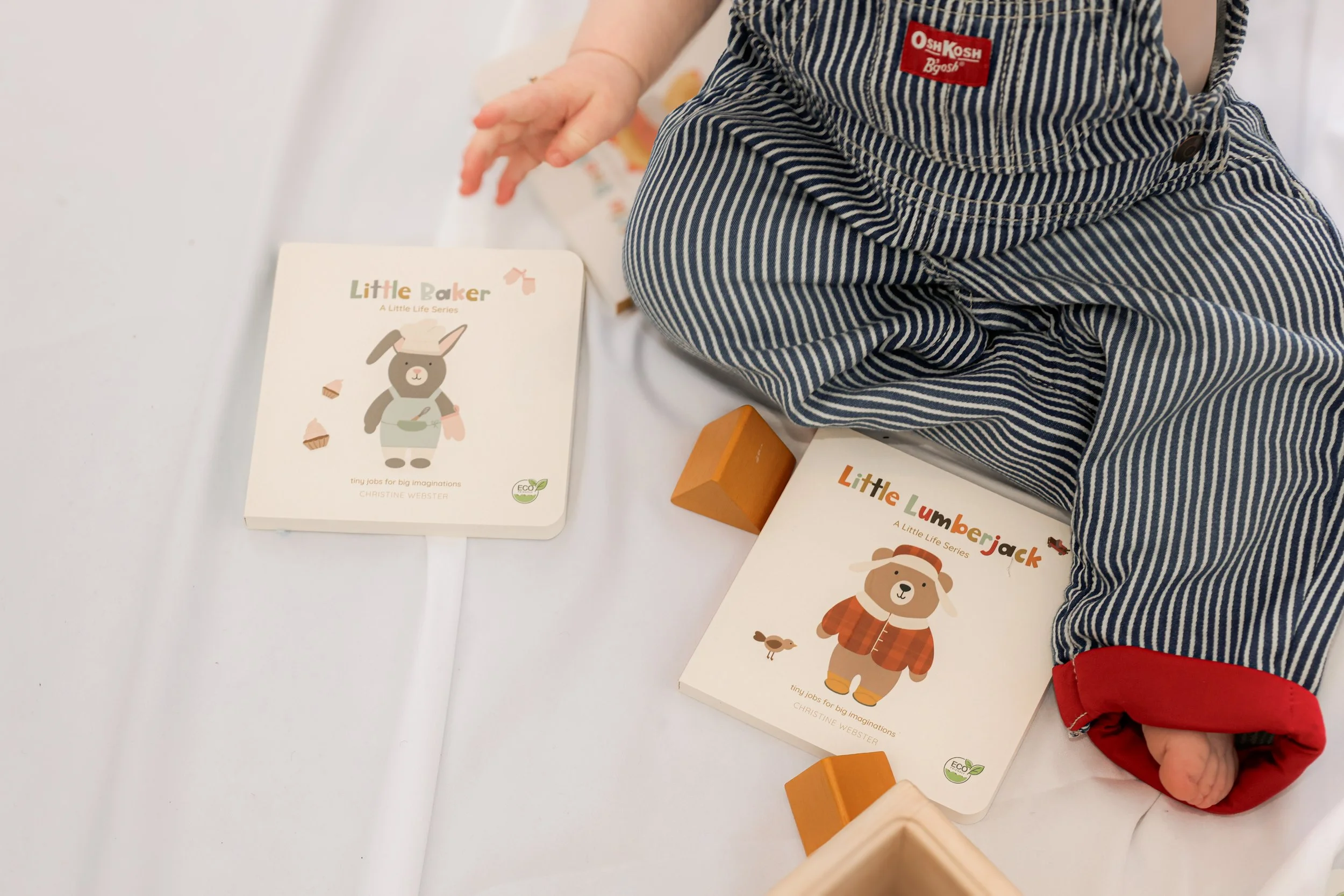 Child with striped clothing sitting next to children's books about animals and a small wooden block on a white surface.