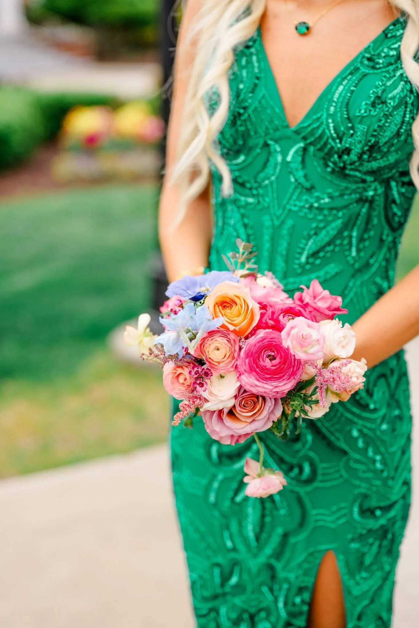 Woman in a green dress holding a bouquet of pink and peach flowers outdoors.