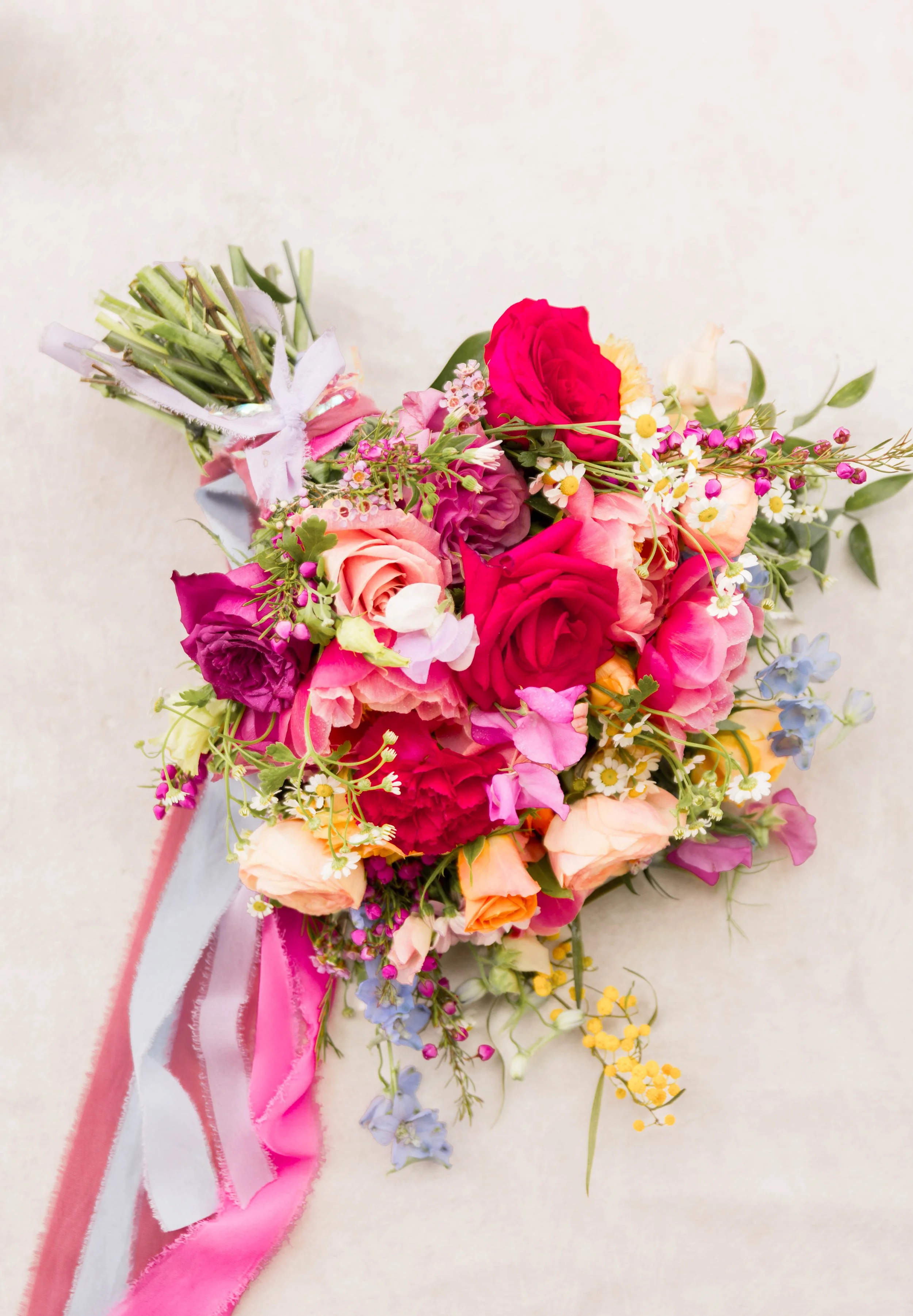 A colorful bouquet of mixed flowers including roses, daisies, and other blooms, decorated with pink and white ribbons.