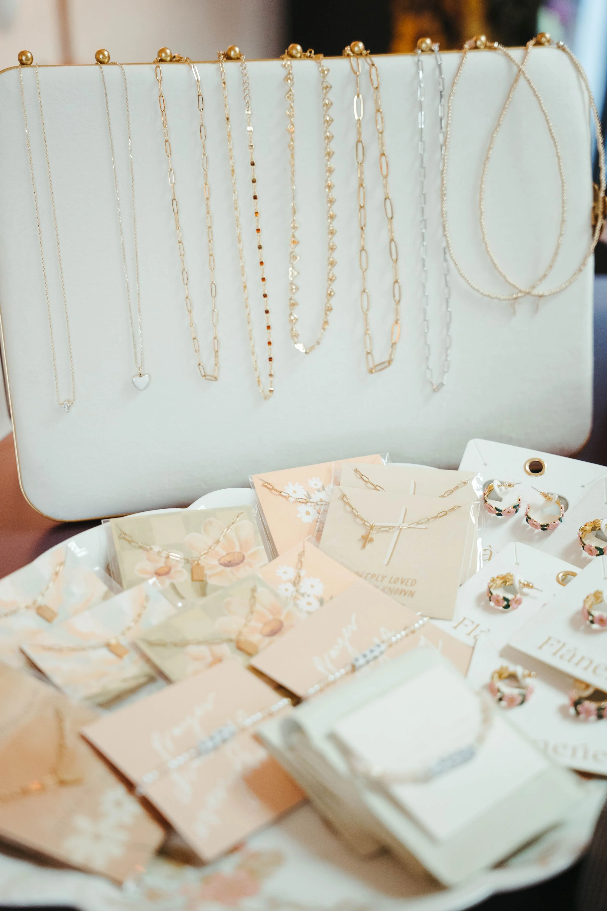 Display of jewelry including necklaces, earrings, and bracelets on a jewelry stand and in packaging, with necklaces hanging on a white board and earrings in small packs.