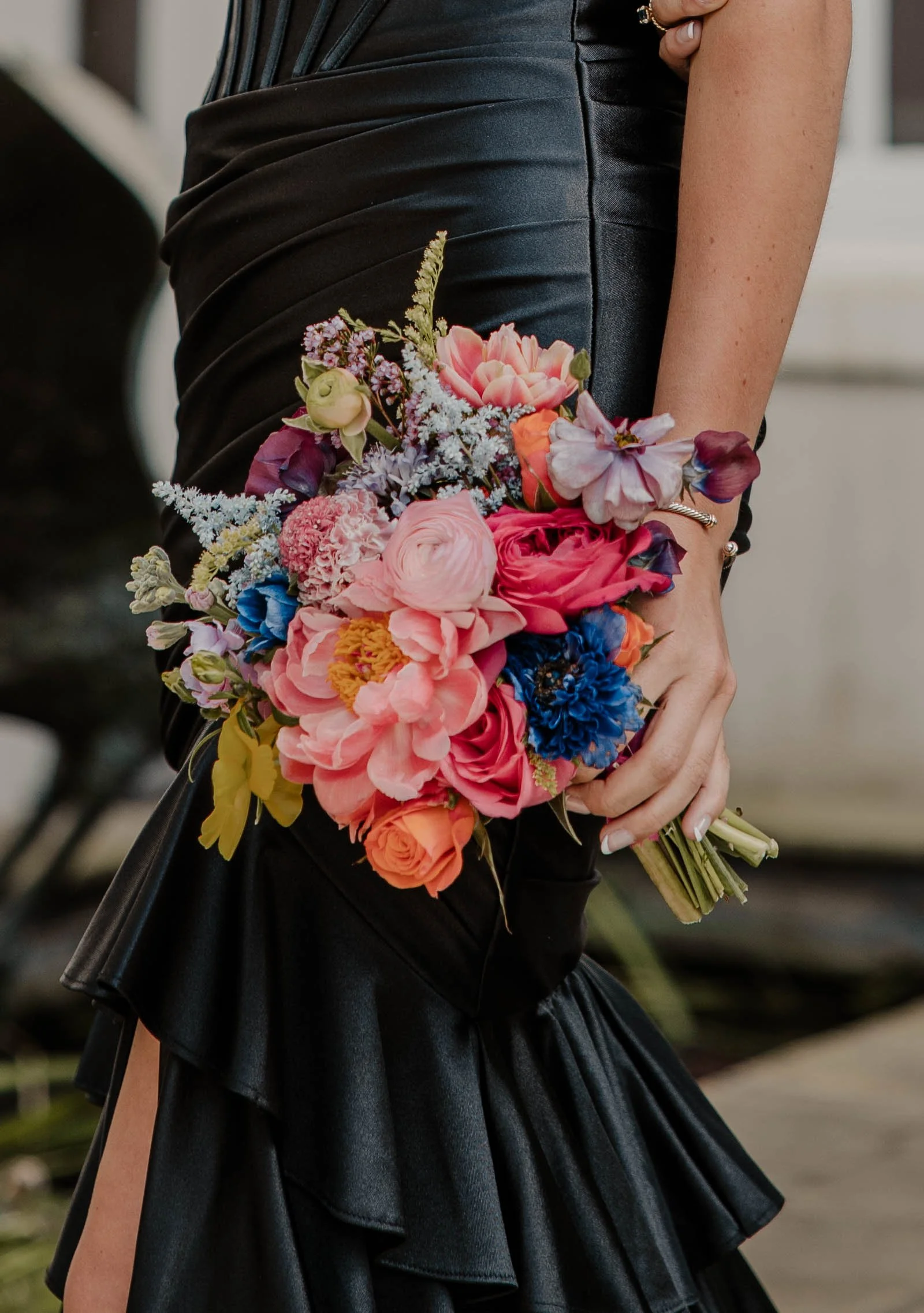A person in a black dress holding a colorful bouquet of flowers.