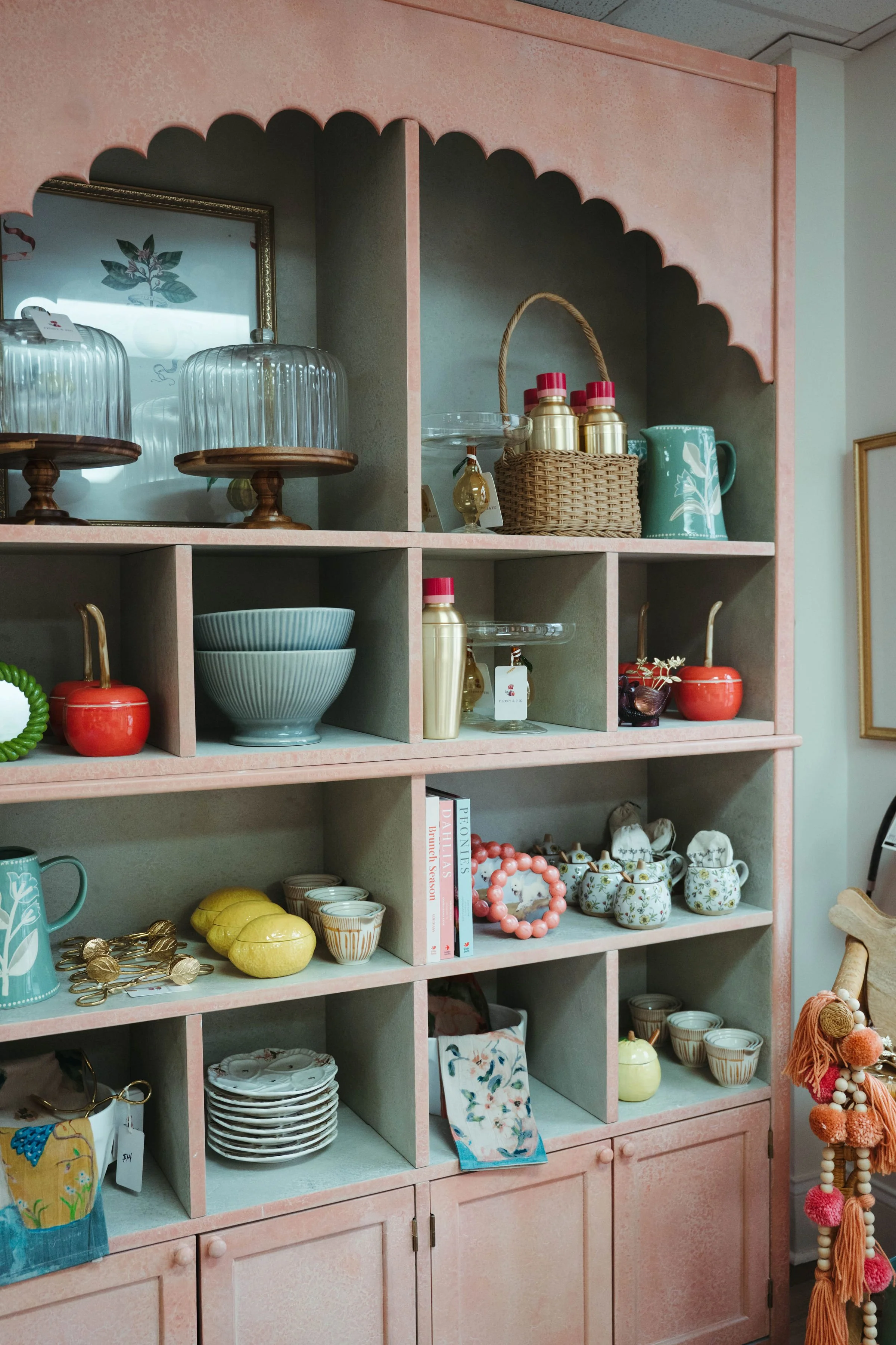 Decorative kitchen hutch with vintage dishes, bowls, and glassware on pink shelves.