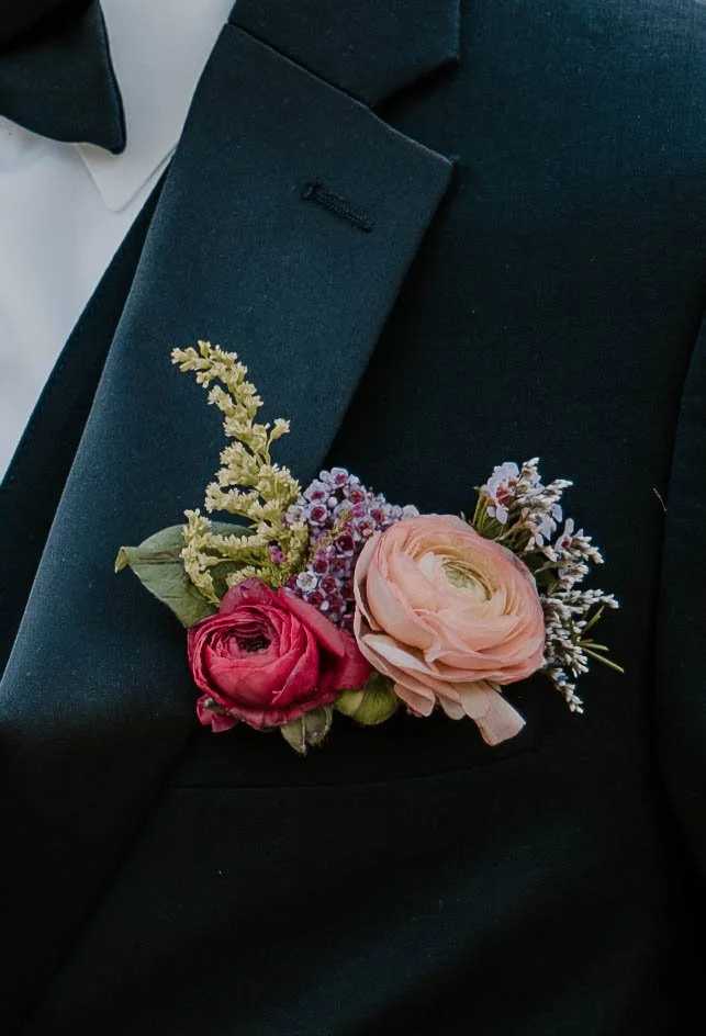 Close-up of a black suit jacket with a boutonniere made of pink and purple flowers pinned to the lapel.