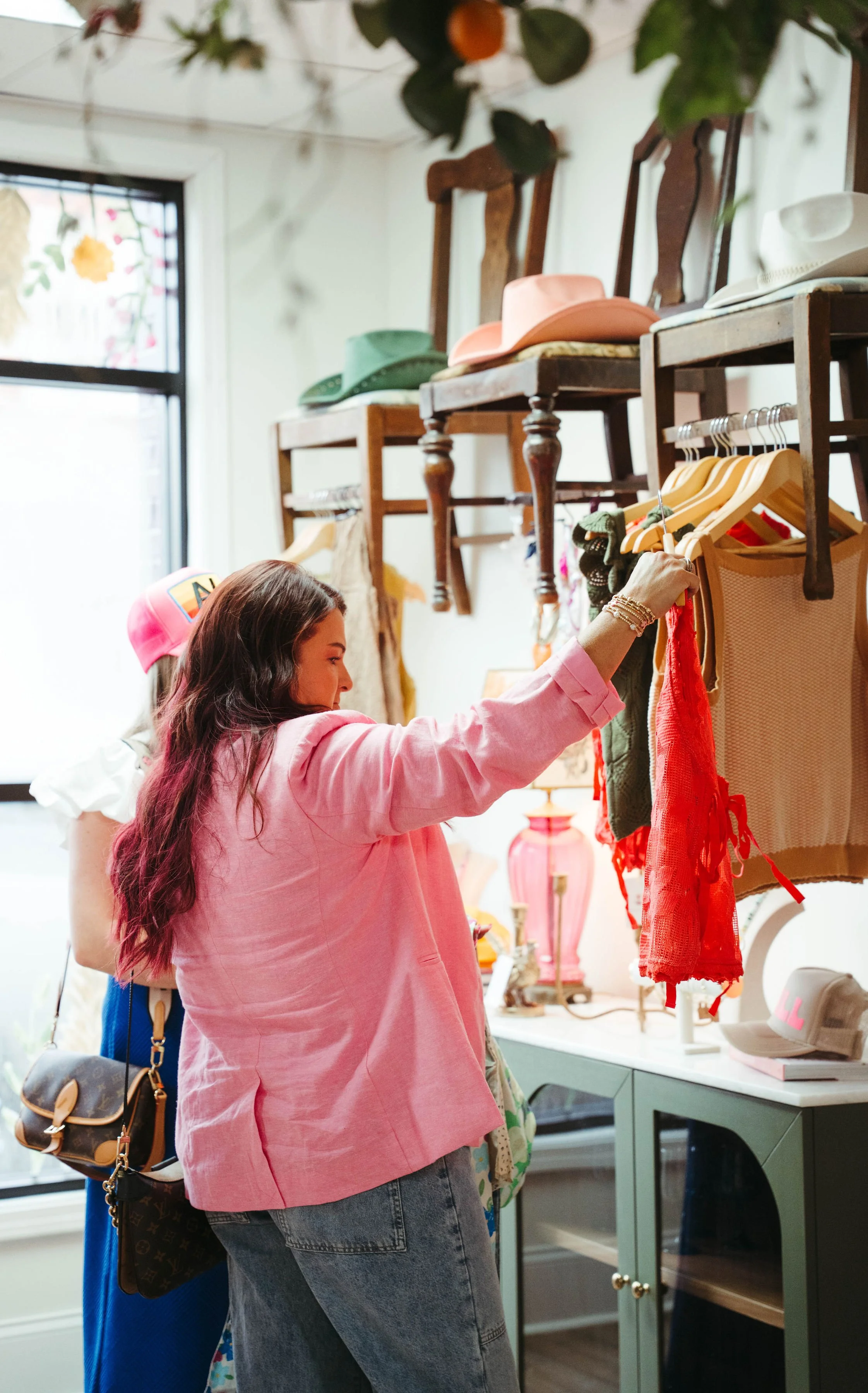 Woman shopping for clothes inside a boutique store, browsing through tank tops on a clothing rack.