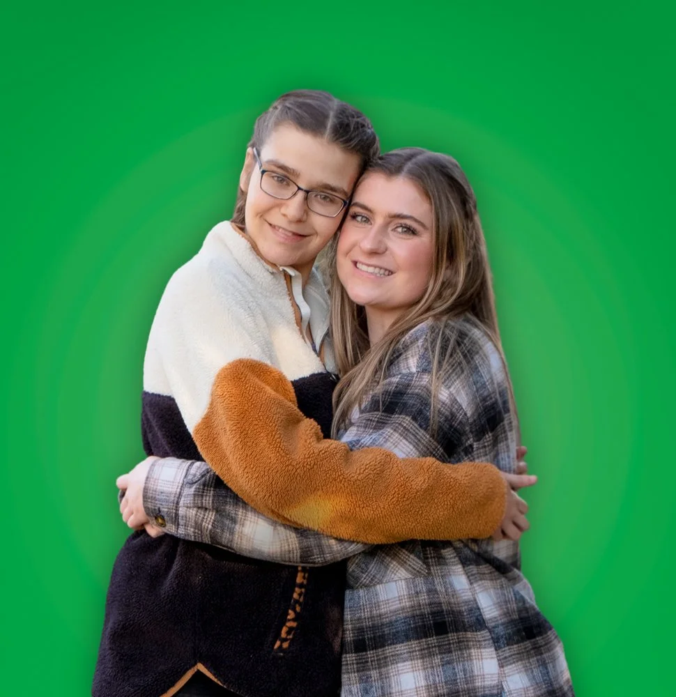Two women hugging and smiling at the camera against a green background.