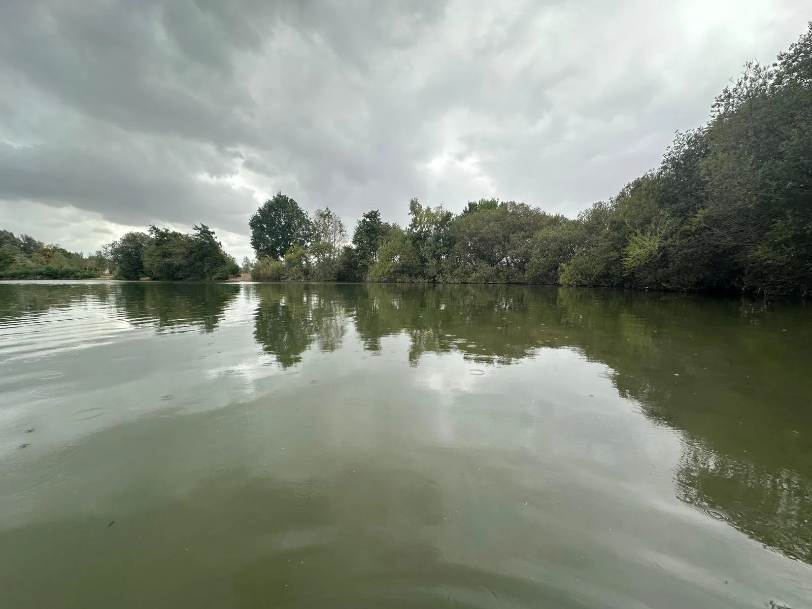 Overcast sky with dark clouds over a calm river, reflecting the surrounding trees and sky.