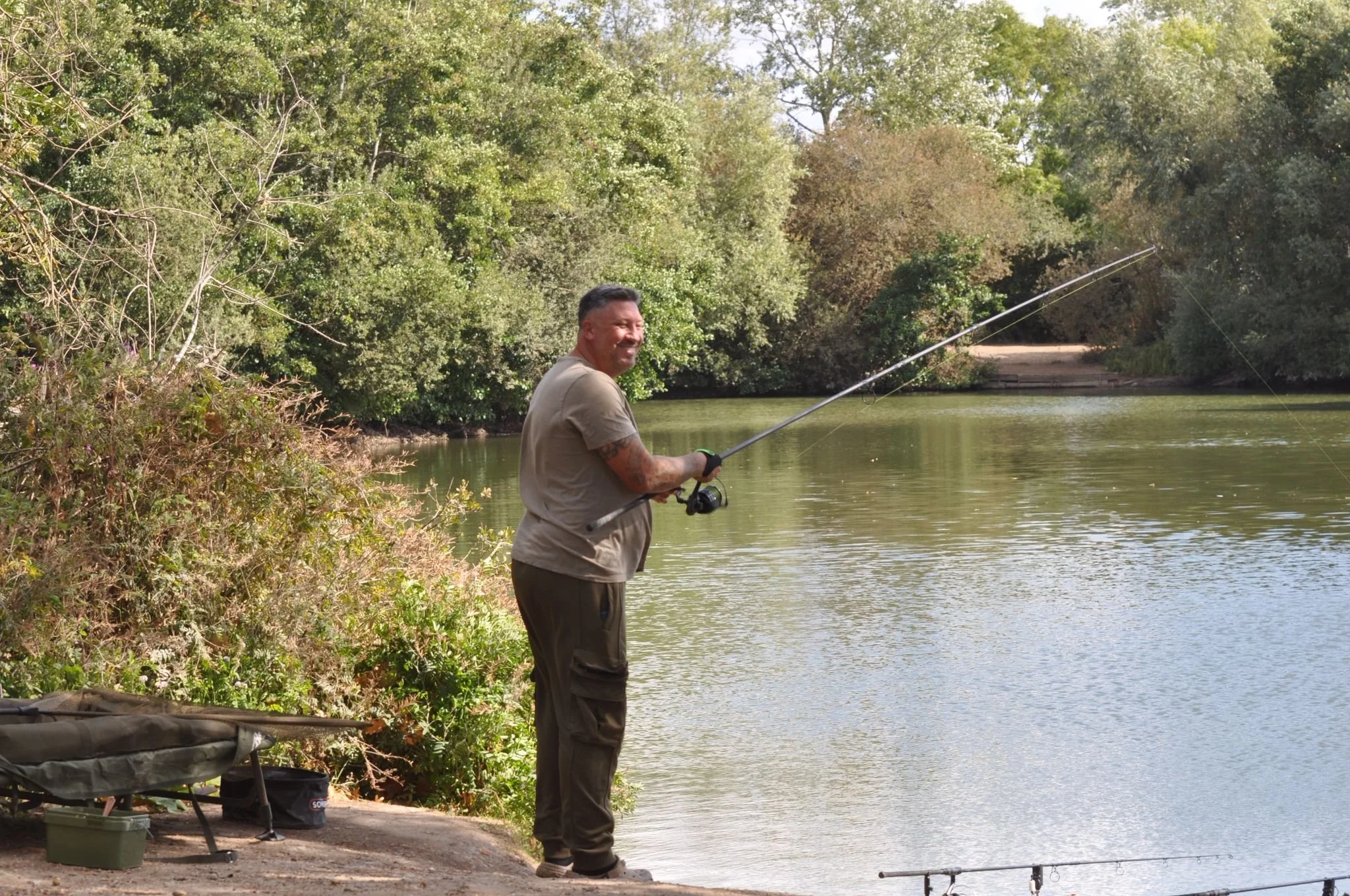 A man standing by a river, fishing with a rod, surrounded by trees and bushes.