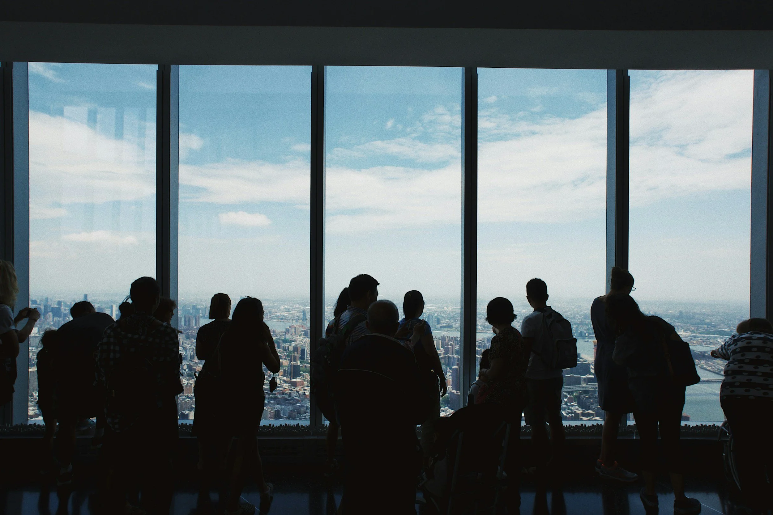 People standing and looking out of large glass windows overlooking a city skyline on a clear day.