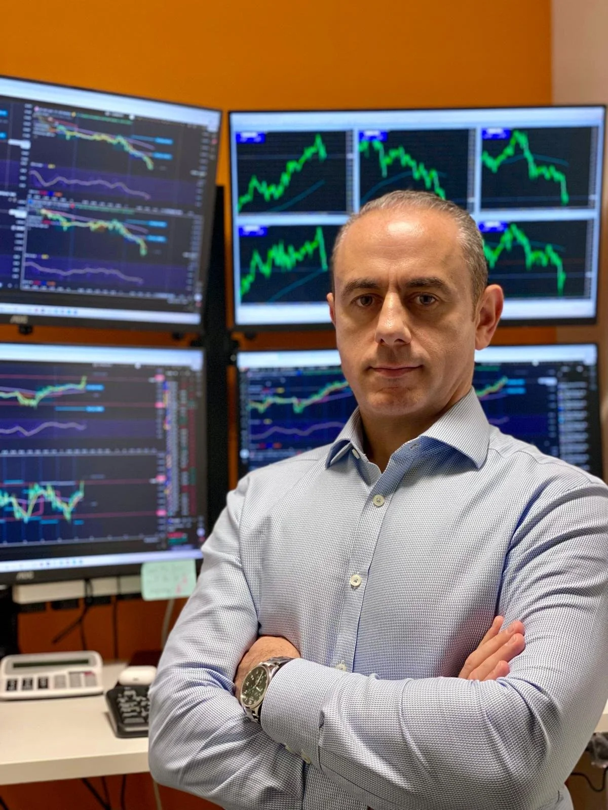 Paul Jannece standing in front of multiple computer monitors displaying stock market charts and graphs.