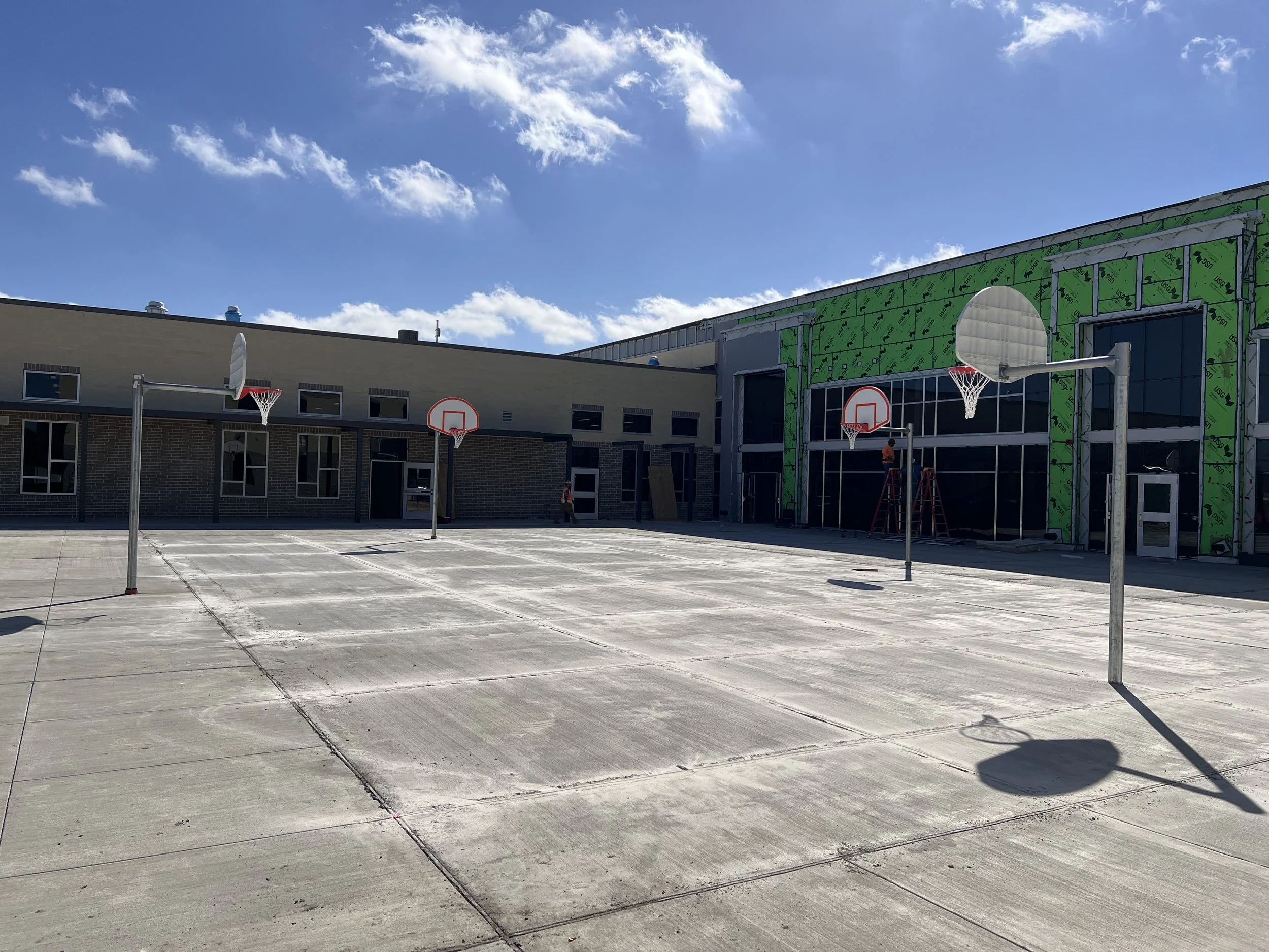 Construction site of an outdoor basketball court at a local Texas school with four basketball hoops and a school under construction in the background.