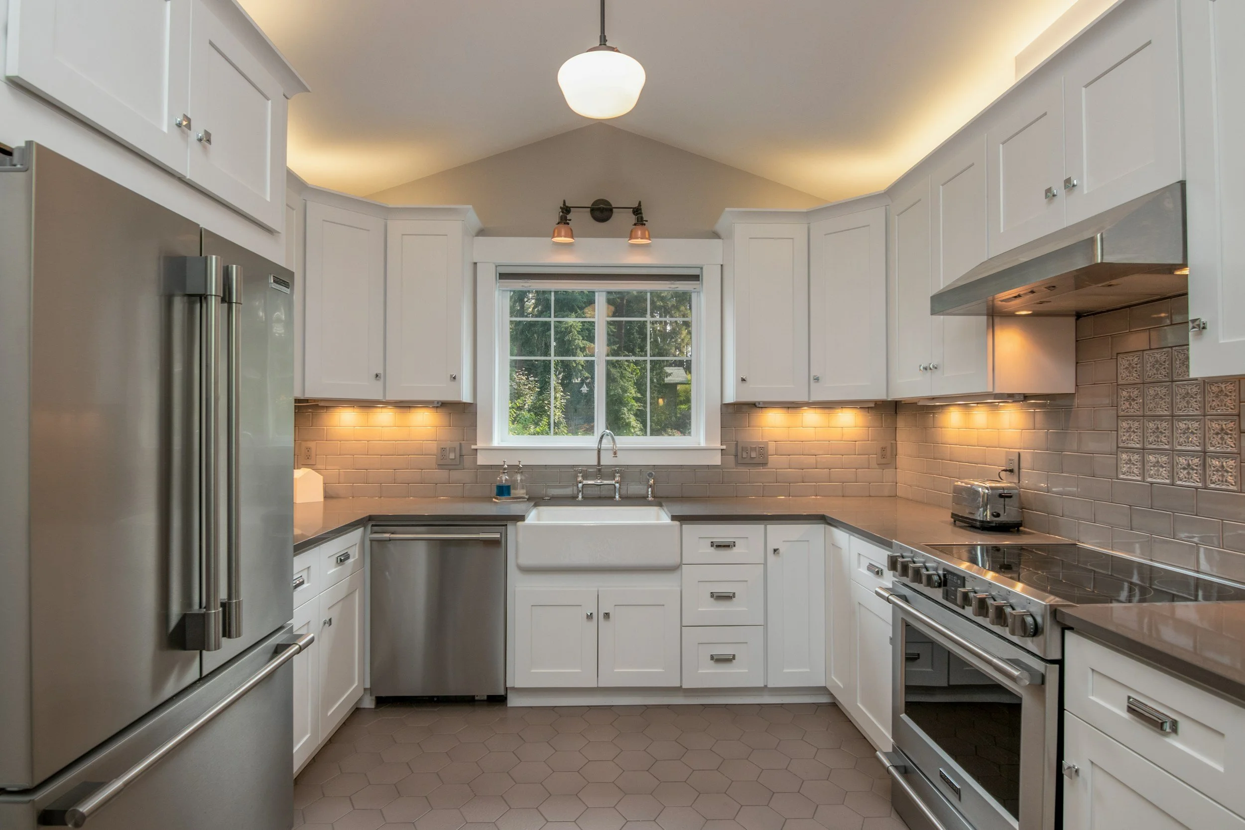 Modern kitchen with white cabinets, stainless steel appliances, hexagon tile floor, beige tiled backsplash, and window above sink