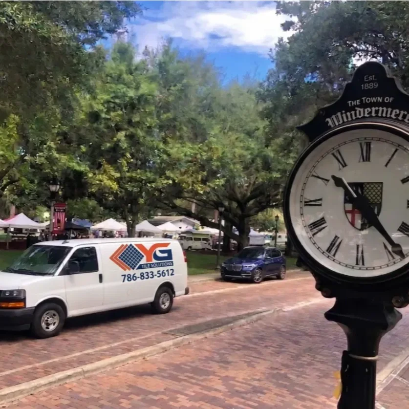 Street scene in Windermere, with a clock showing 10:26, a white van labeled 'YC Tile Solutions,' parked cars, and trees lining the street.