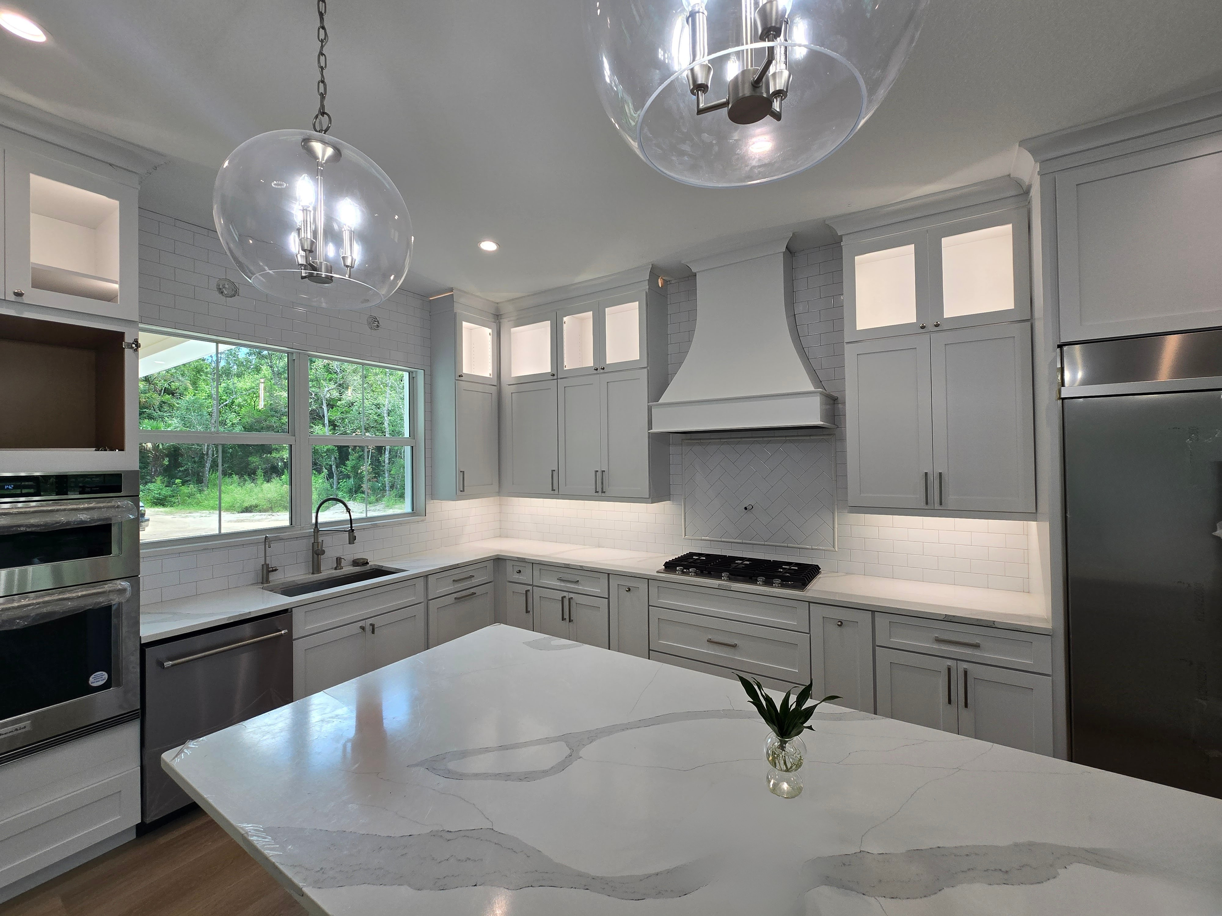 Modern kitchen with white cabinets, marble island, large window, stainless steel appliances, and white subway tile backsplash.