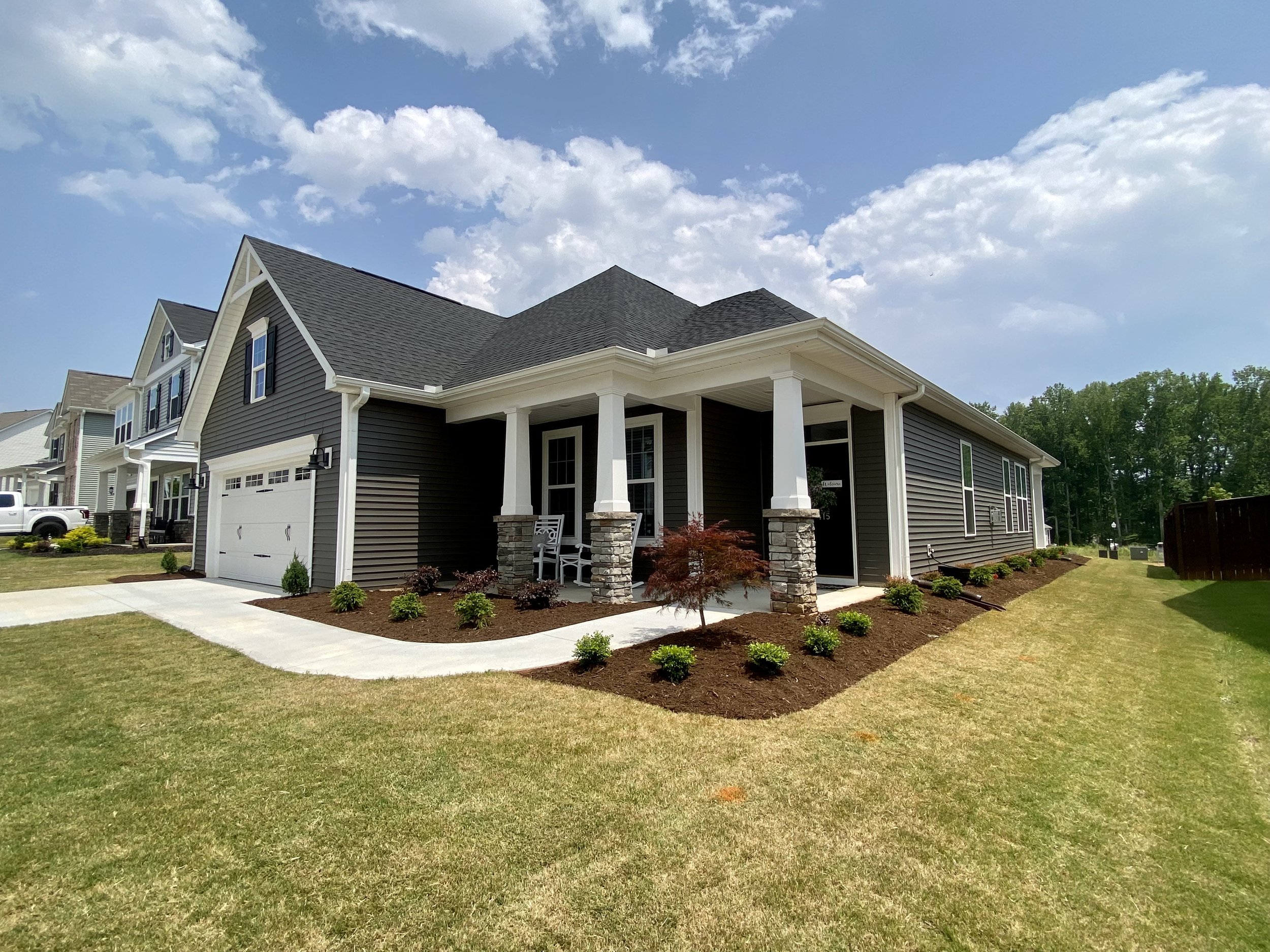 Modern two-story house with dark gray siding, white trim, and a front porch supported by white columns, with a well-maintained lawn and driveway on a sunny day.