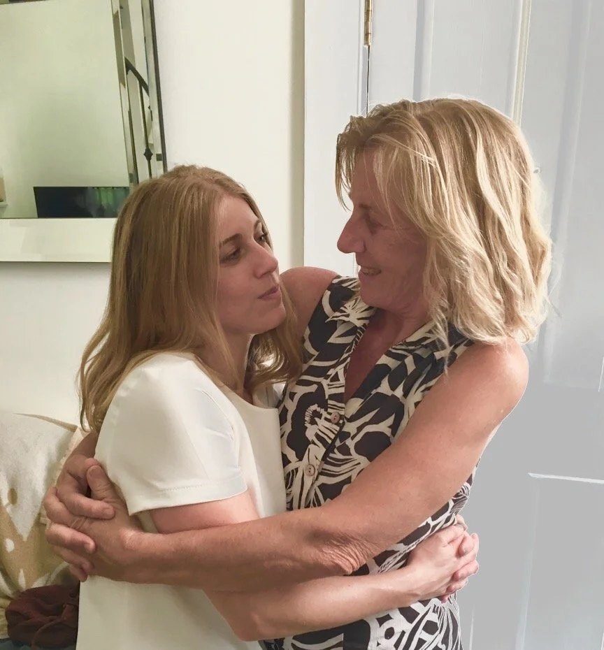Mother and daughter are hugging and smiling at each other warmly.