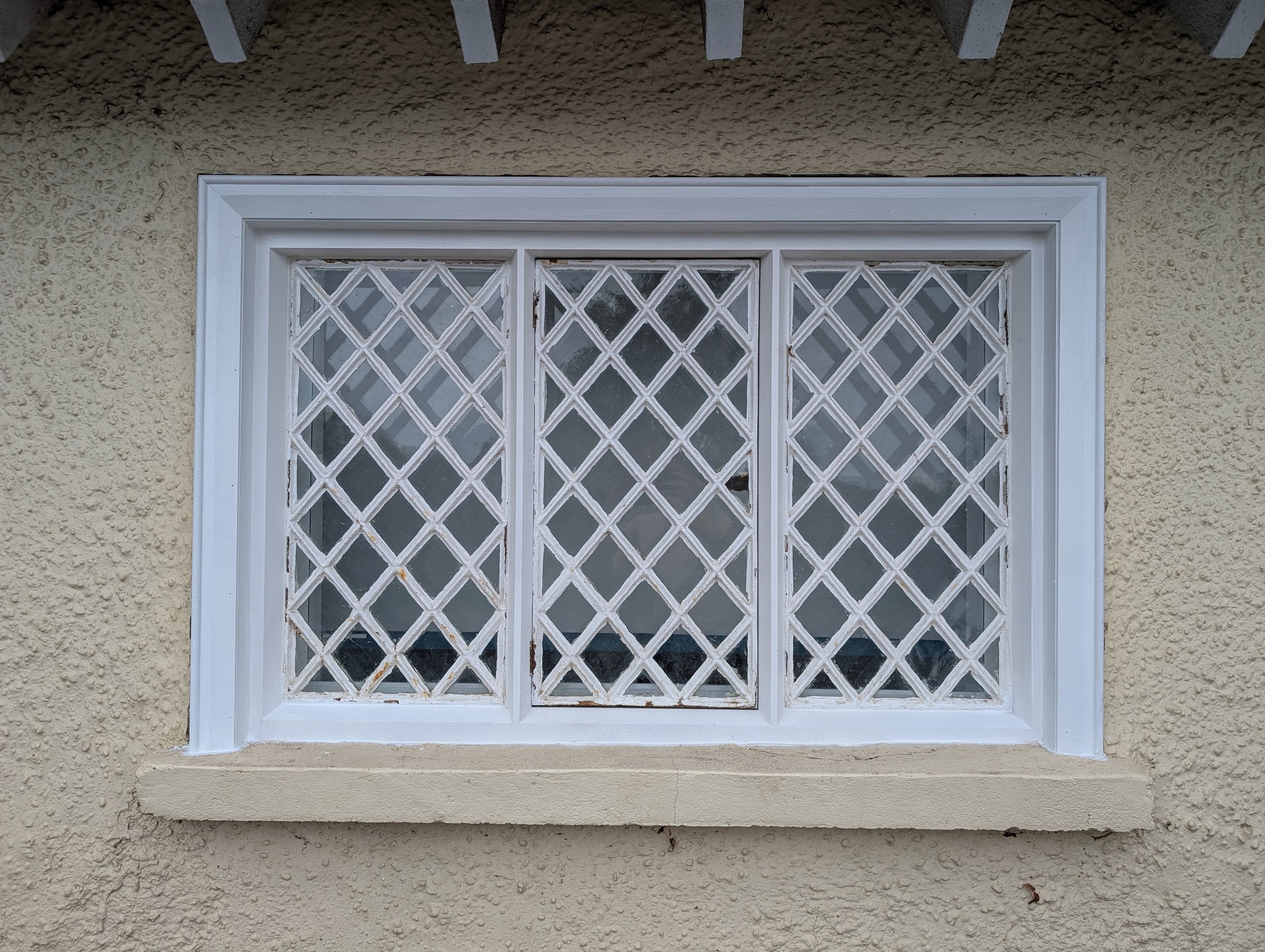 A rectangular window with a white frame and decorative lattice security bars on the exterior of a beige stucco wall.