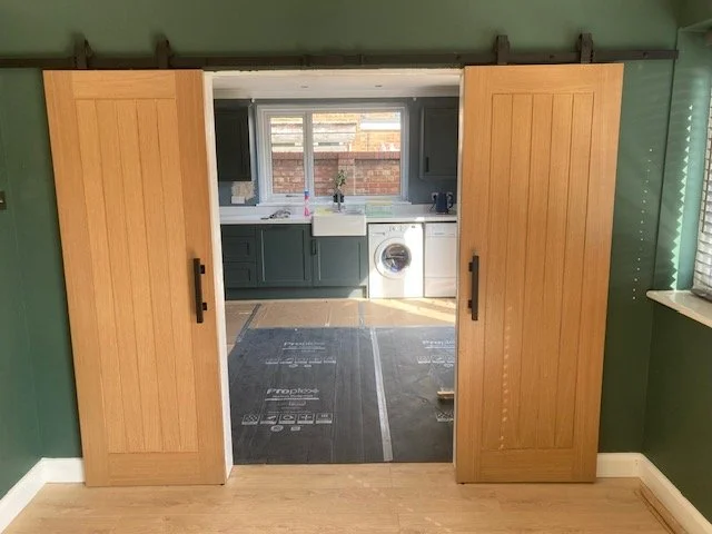 Wooden barn doors opening to a laundry room with washing machine and sink in a home interior.