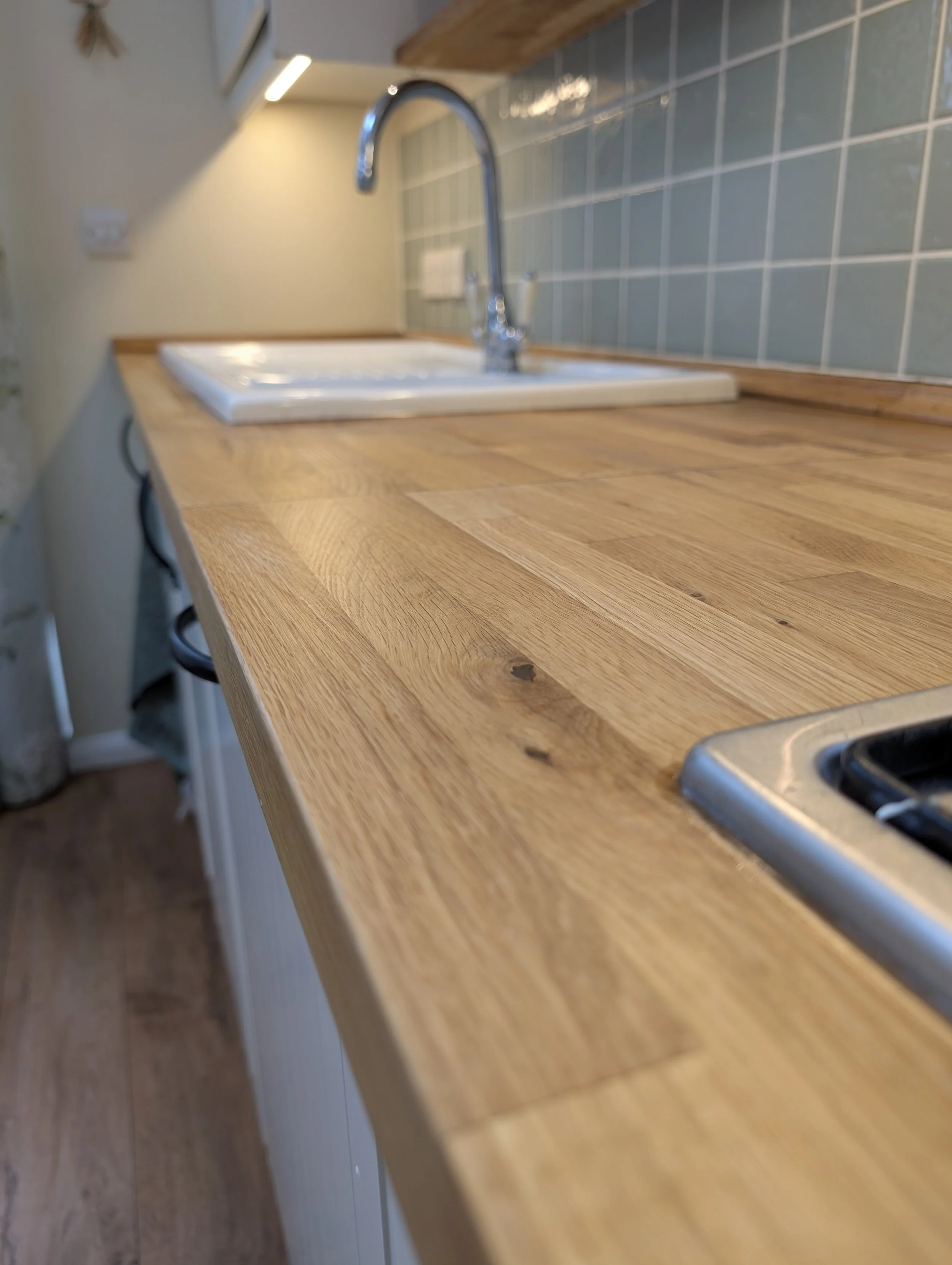 Close-up view of a wooden kitchen countertop with a built-in sink and a chrome faucet. Tiled backsplash and upper cabinets are visible in the background.