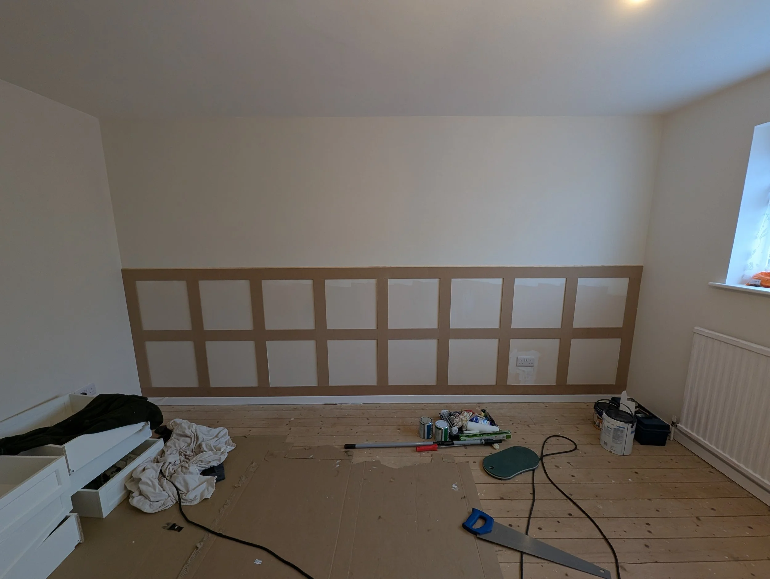 Room under renovation with a partially painted wall, paint supplies, and tools on the floor.