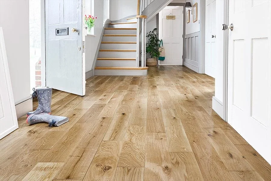 A bright entryway with wooden flooring, a staircase with white risers, a door with a mailbox, and a pair of children's boots on the floor.