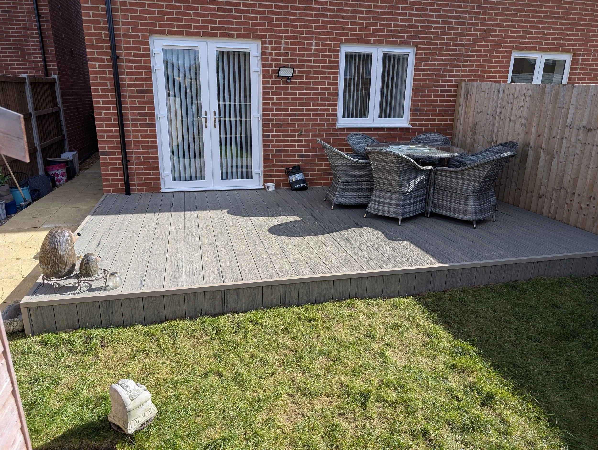 Backyard patio with wicker dining set, glass doors, and a grass lawn.