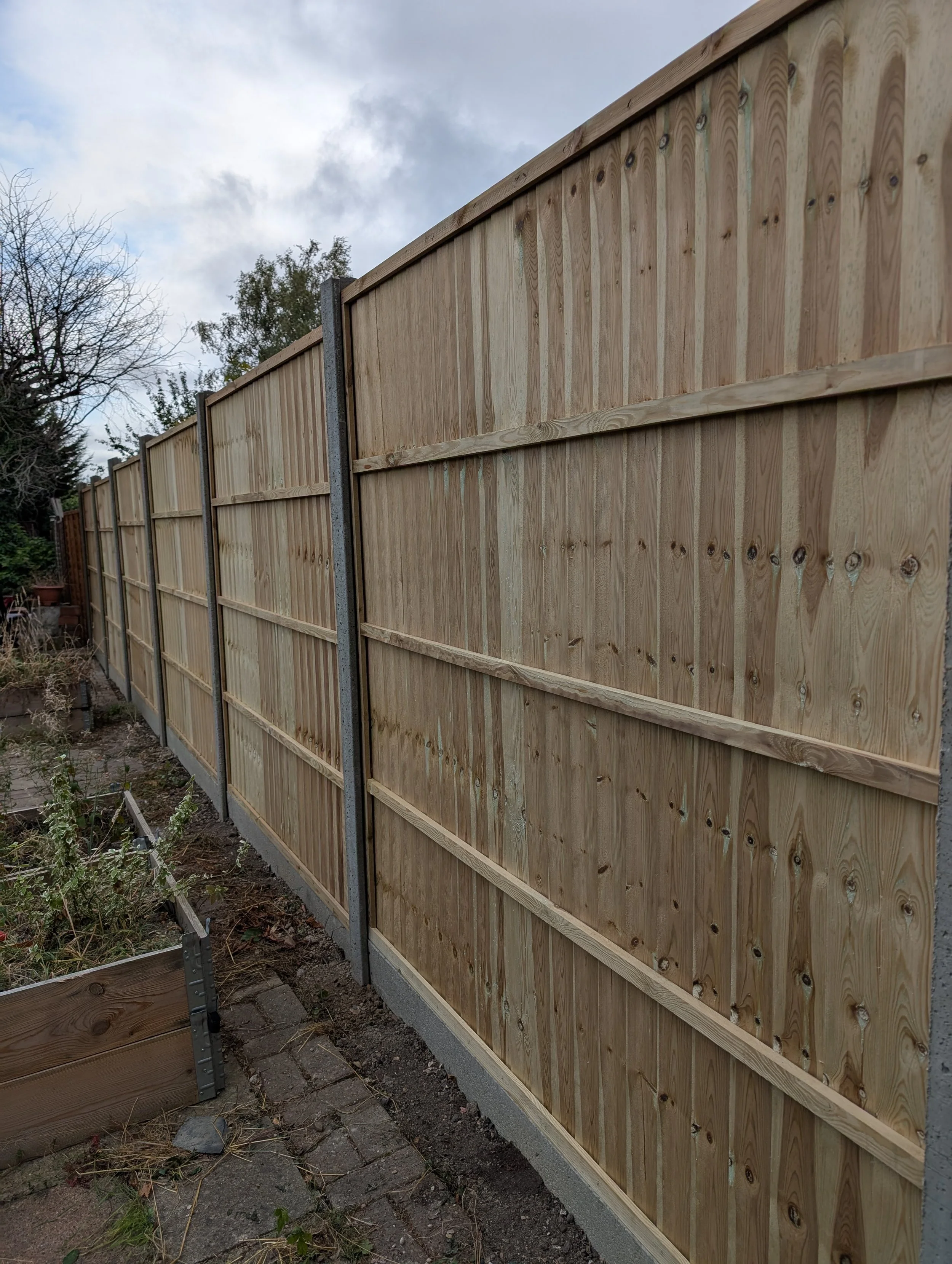 New wooden privacy fence in a backyard with plants and garden beds nearby.