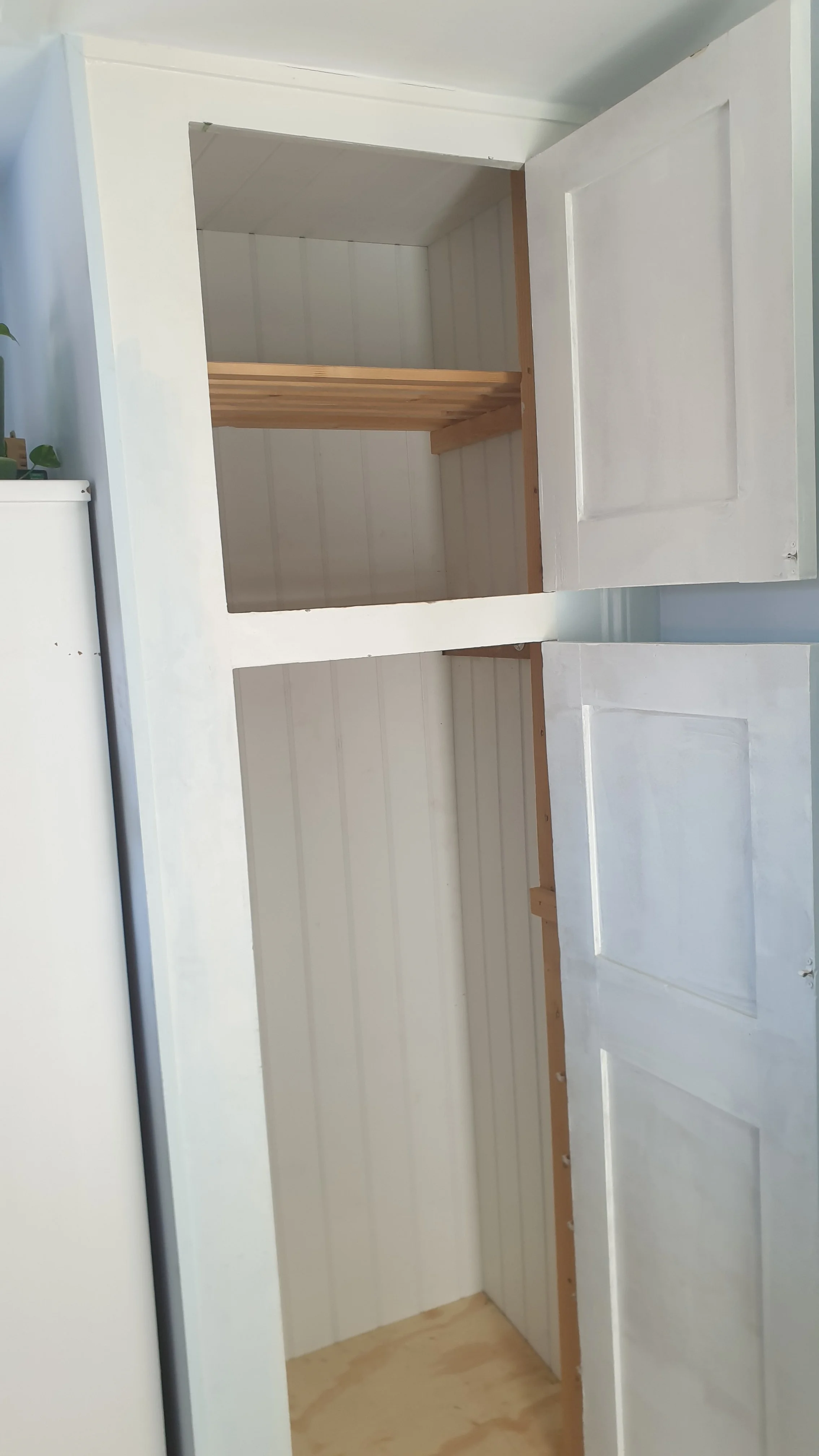An unfinished white wooden cabinet with open doors revealing two shelves inside.