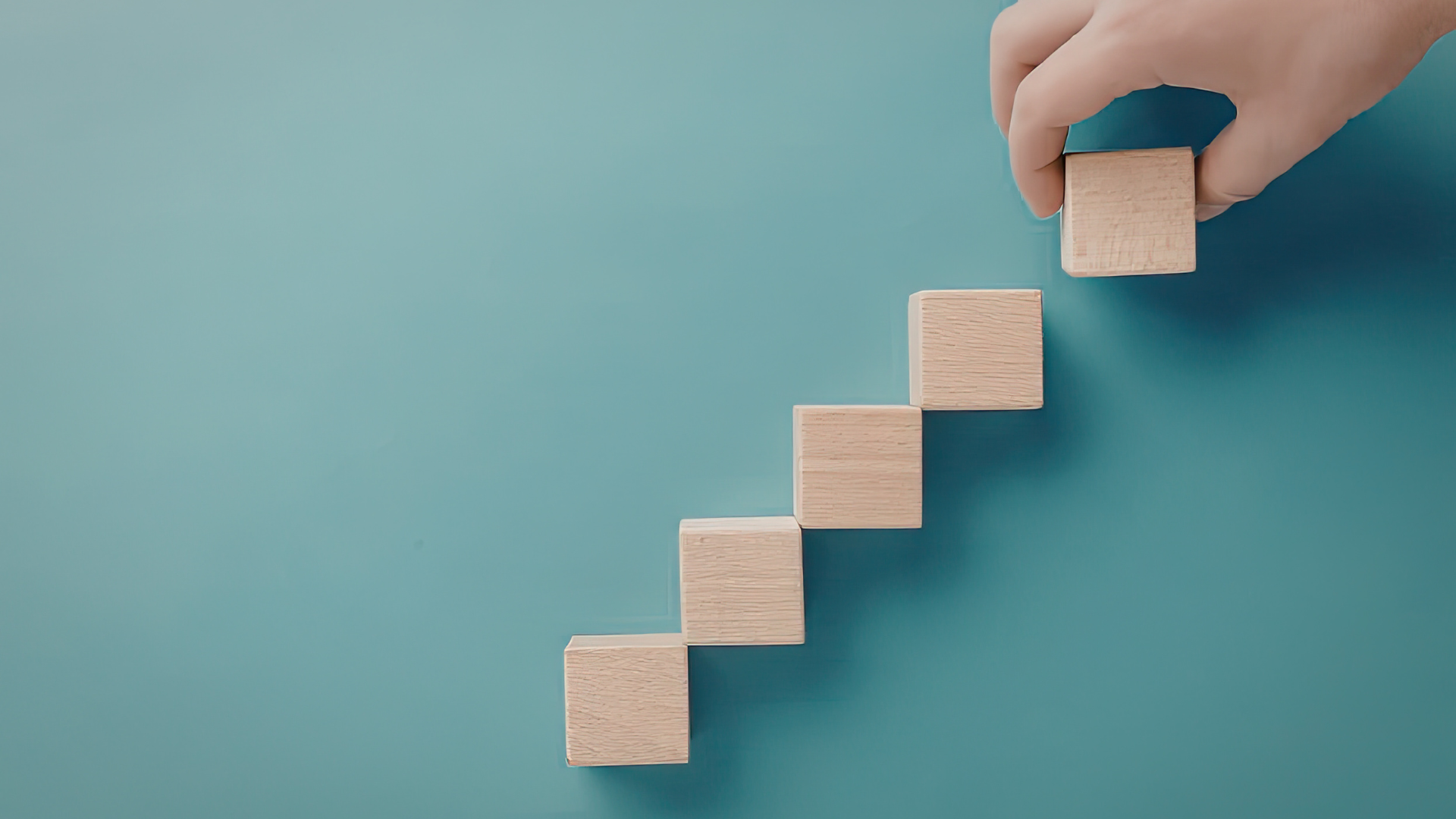 Hand legt Holzquadrate in einer aufsteigenden Anordnung auf einem blauen Hintergrund.
