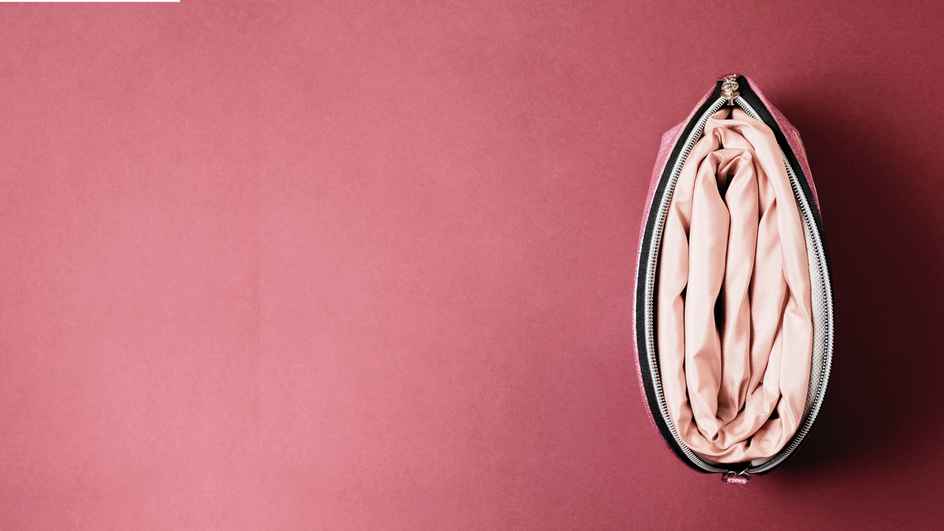 Eine offene, pinke Kosmetiktasche mit cremefarbenem Innenraum auf rosa Hintergrund.