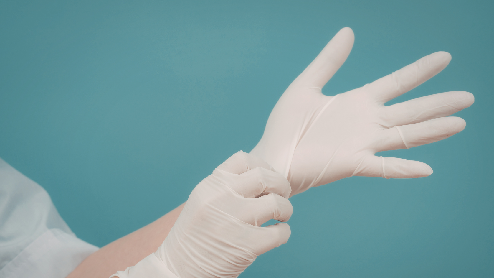 Person zieht eine weiße medizinische Handschuh an, nahe am Handgelenk, vor einem blauen Hintergrund.