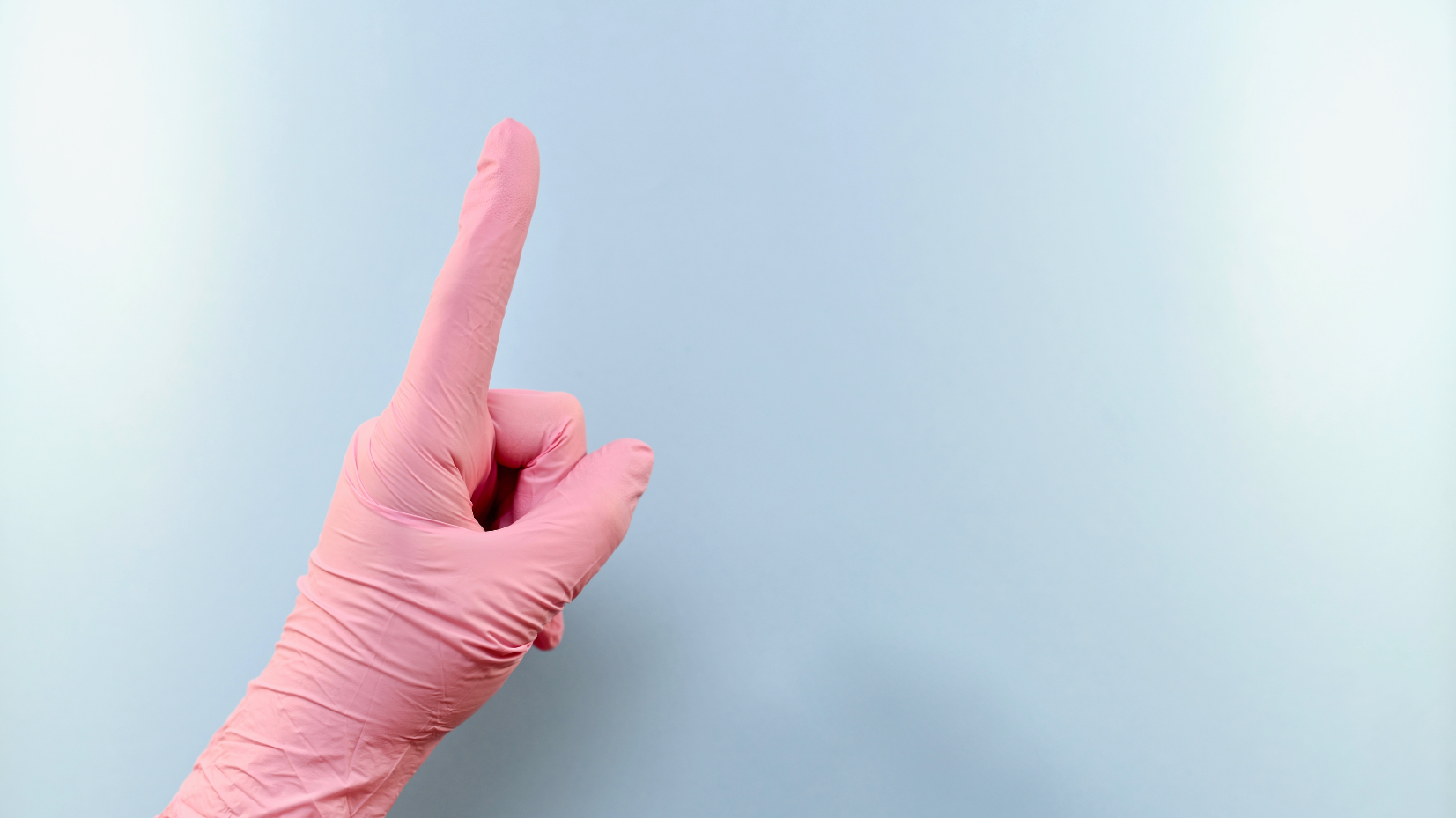 Hand in rosa Gummihandschuh zeigt mit ausgestrecktem Zeigefinger nach oben vor hellem blauen Hintergrund.