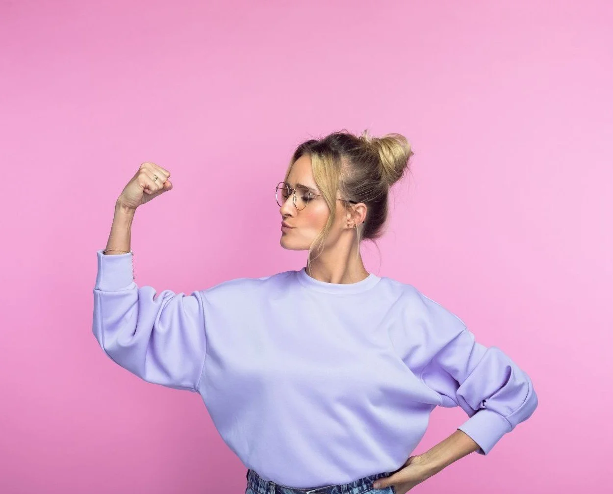 Frau mit Brille posiert pokert vor pinkem Hintergrund, zeigt Muskeln