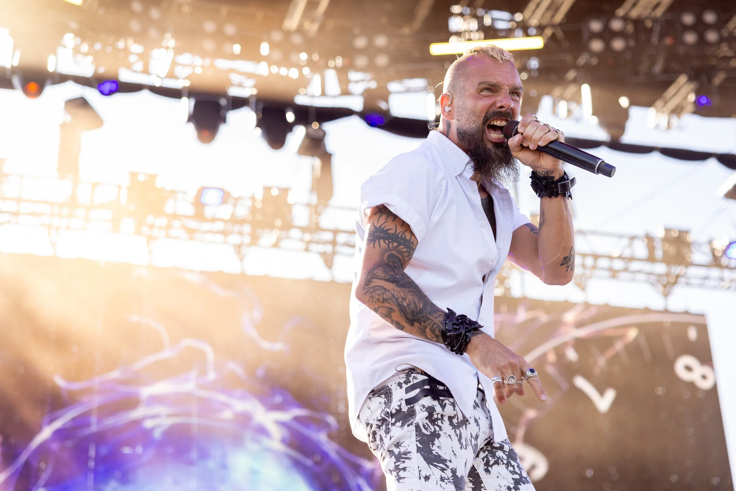 The bright sun nearly completely blows out the background as the singer is clear and well defined, wearing a white shirt and white with black pants, singing into a microphone
