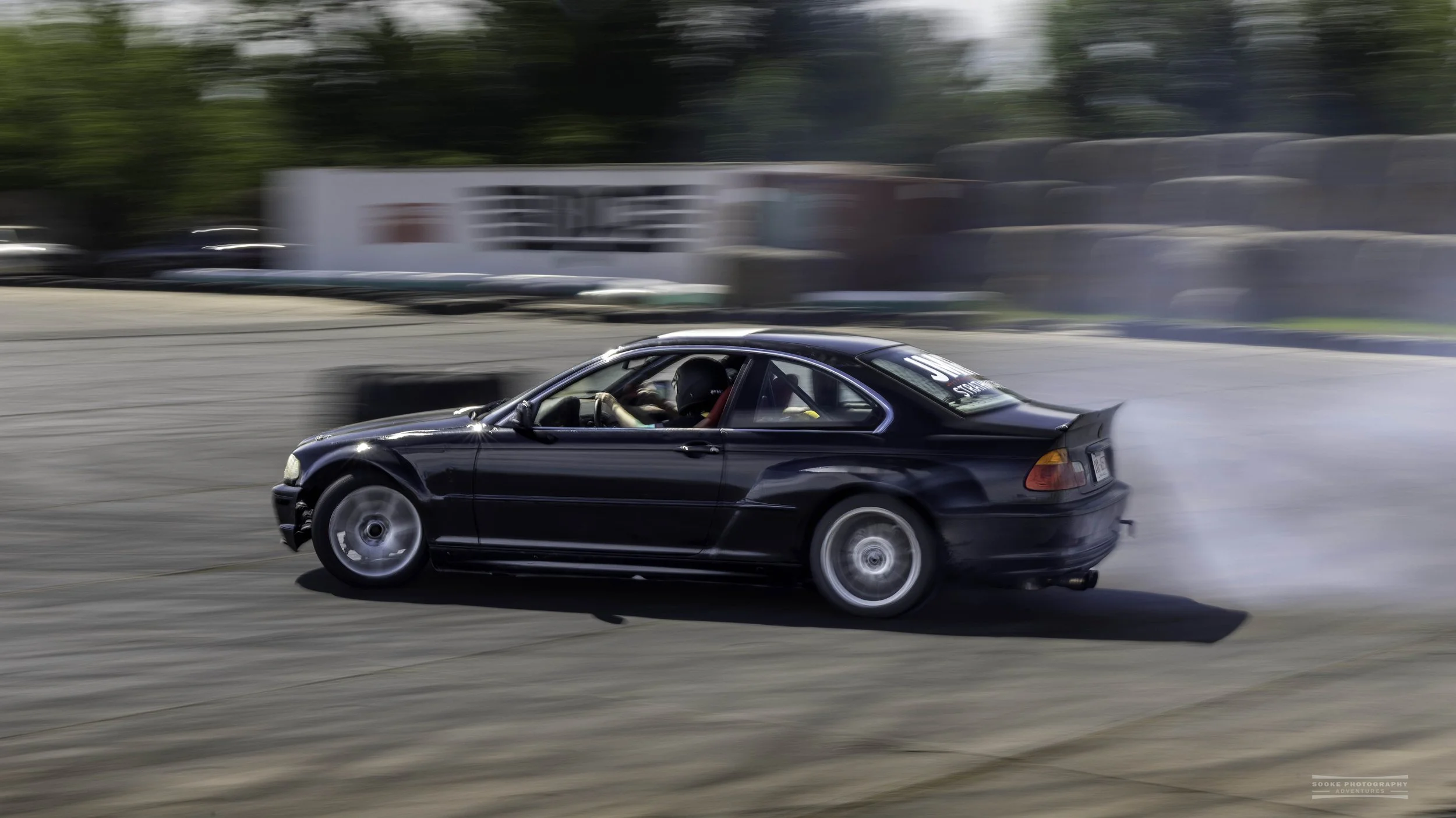 a black BMW in sharp focus, drifts past a large tire at the Rocky Mountain Drift Club