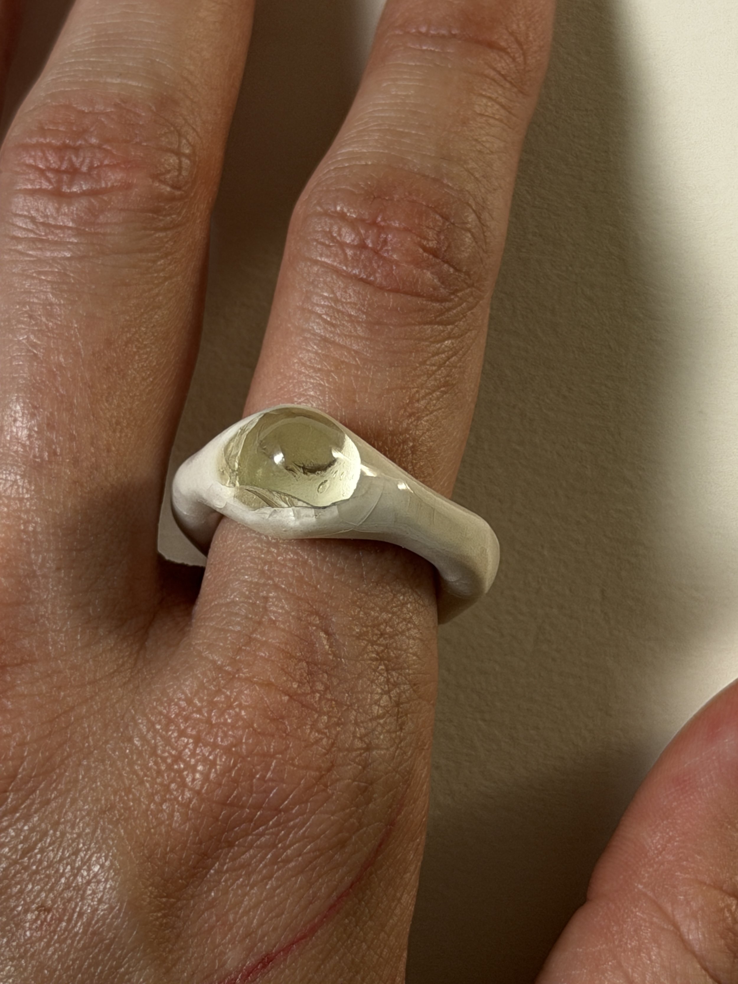 Bone-white porcelain ring with crackle surface worn on hand, central glass jewel visible, close-up