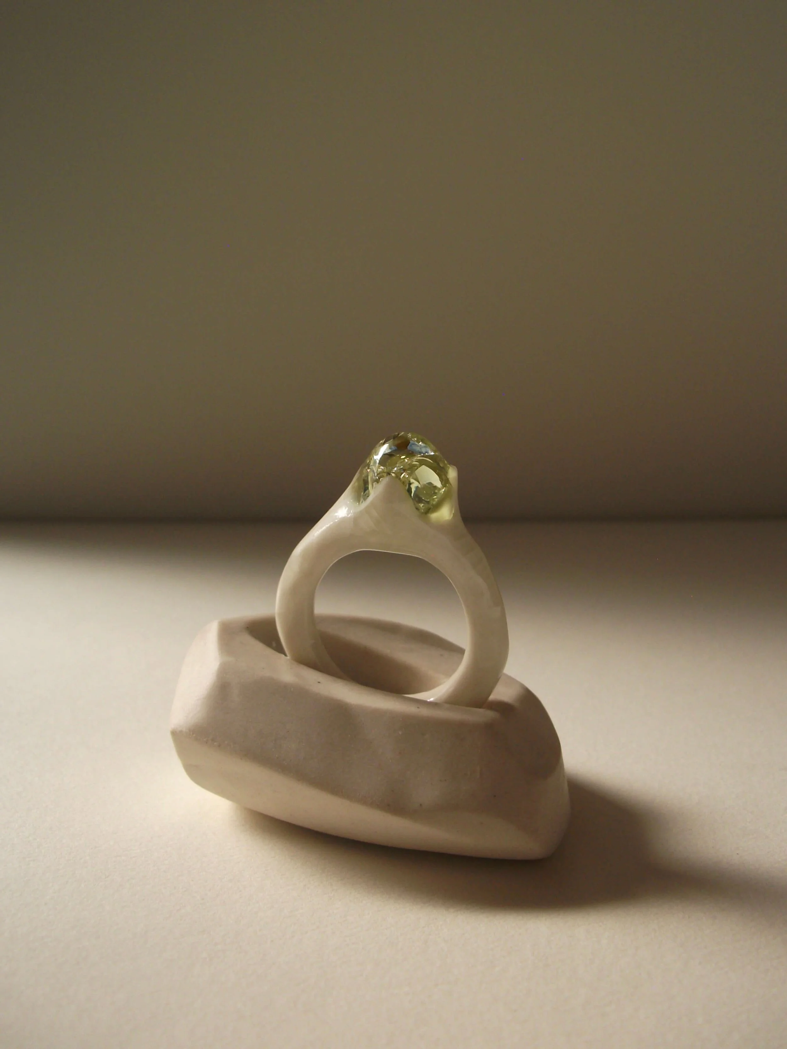 Angled view of bone-white porcelain ring with thin band and glass droplet