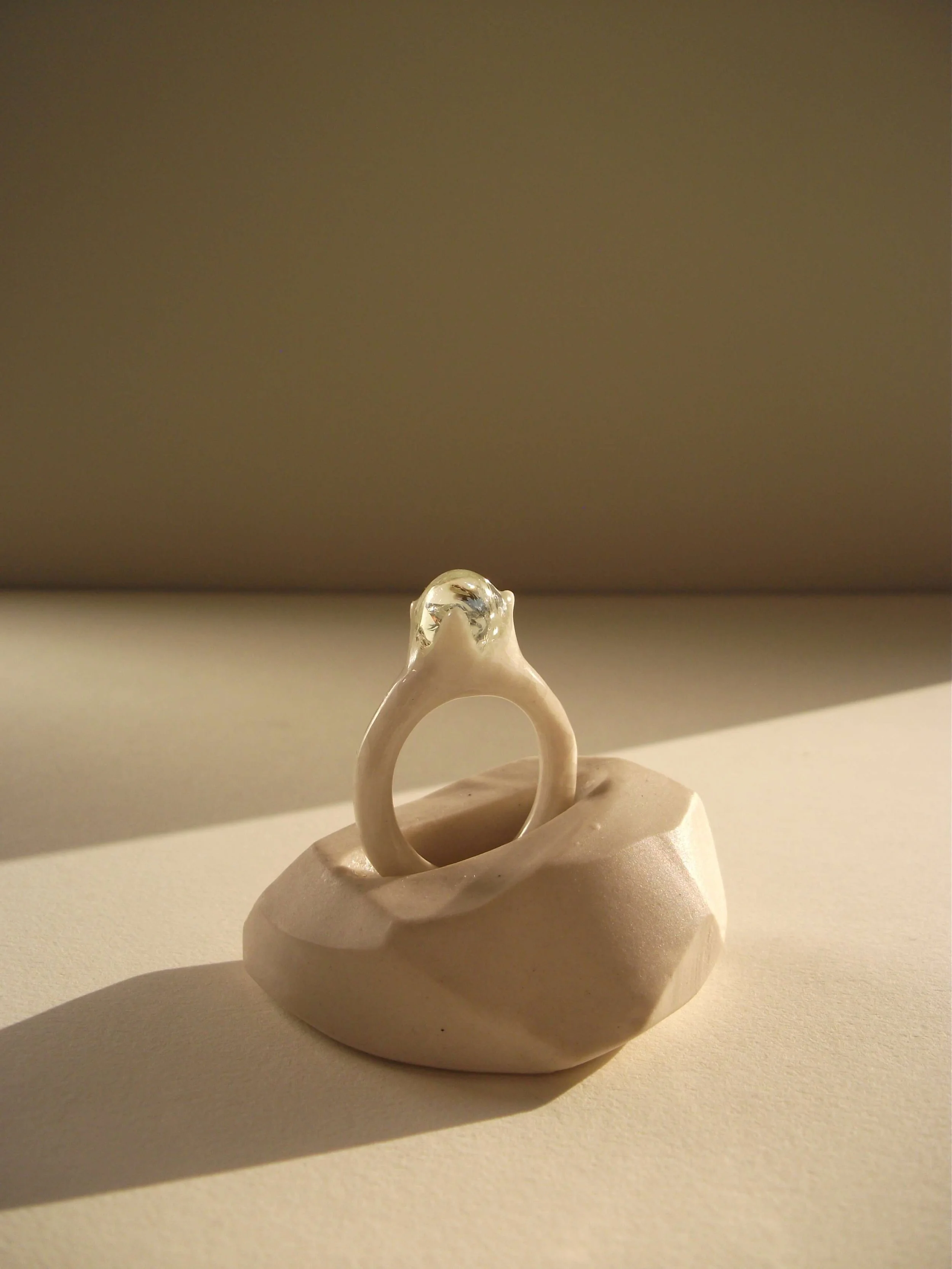 Bone-white porcelain ring with delicate thin band and single glass droplet at crown