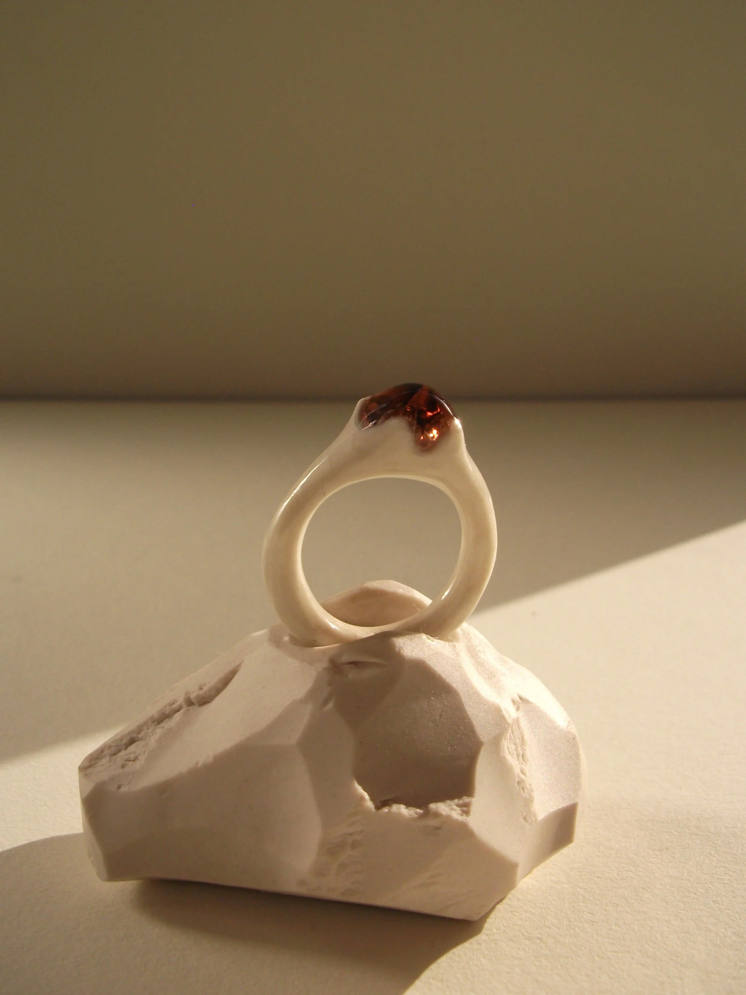 Bone-white porcelain ring with thin delicate band and crimson glass droplet at center