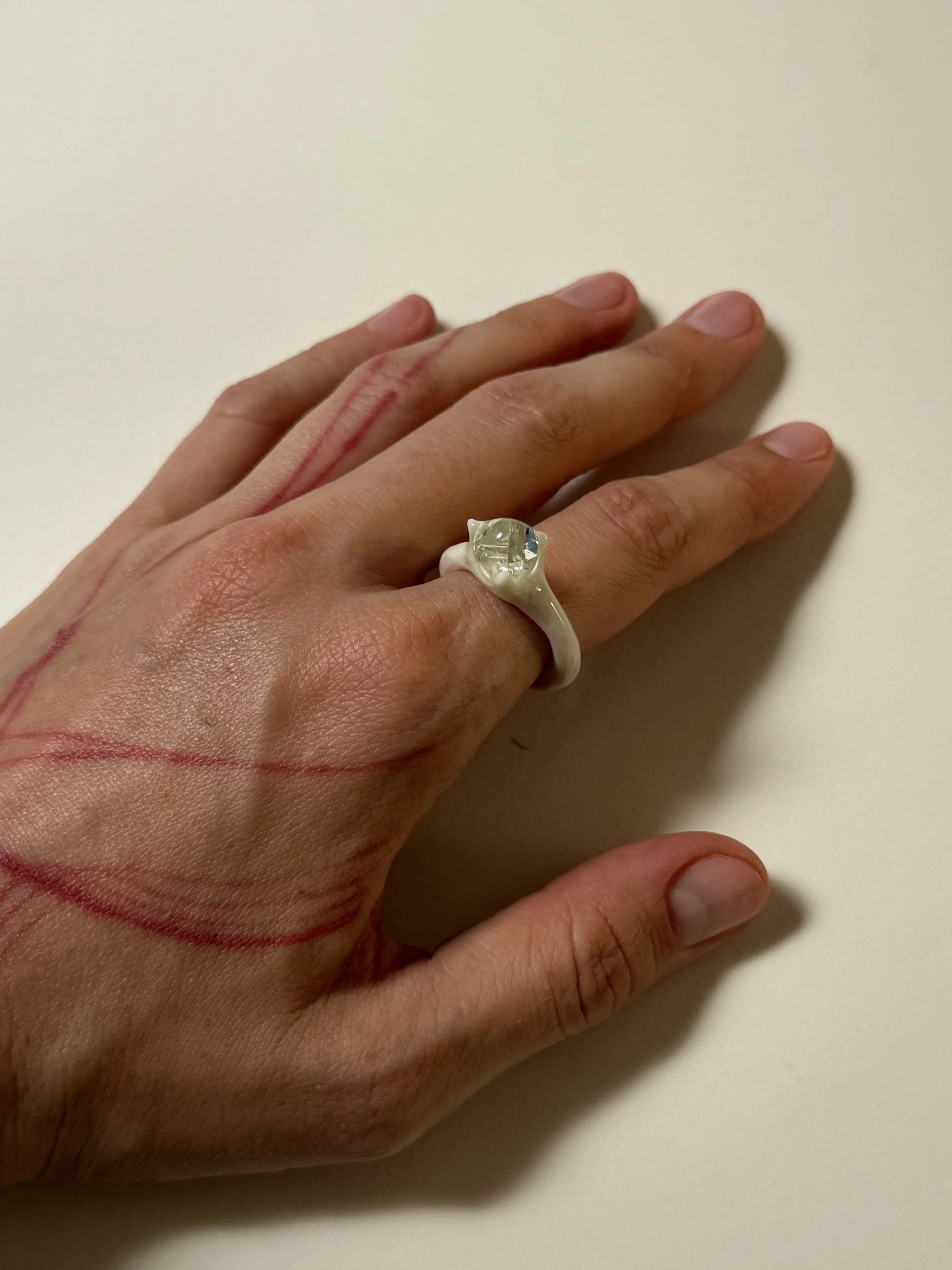 Bone-white porcelain ring with thin band worn on hand, glass droplet visible