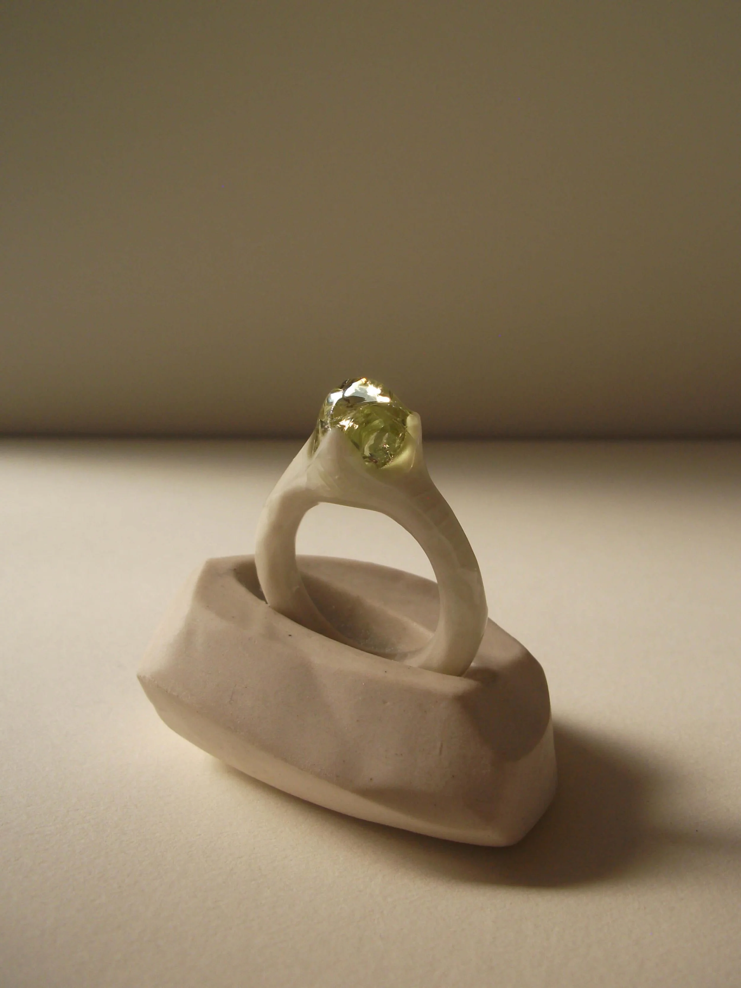Angled view of bone-white porcelain ring with thin band and glass droplet