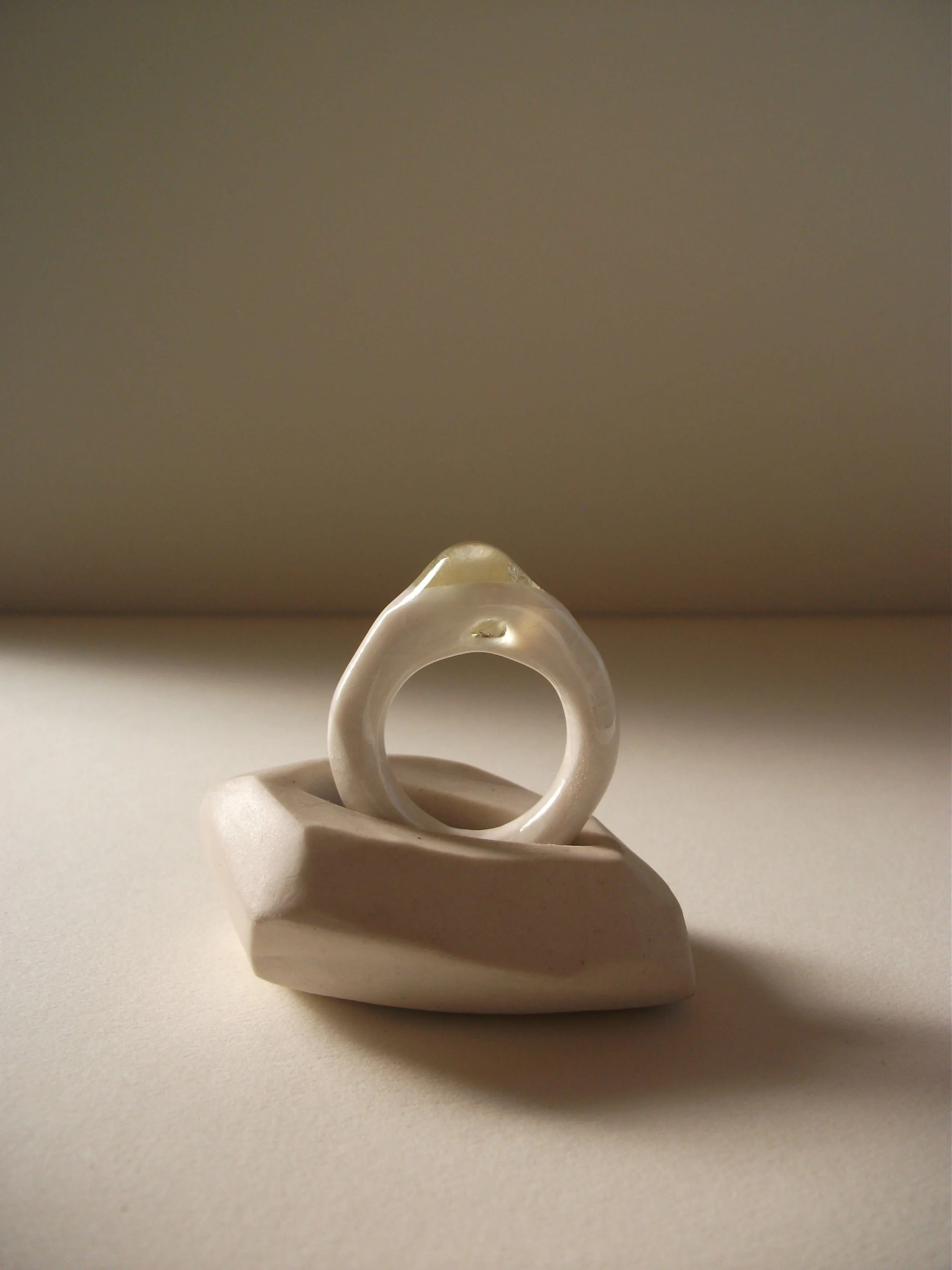 Angled view of bone-white porcelain ring with crackle surface and central glass jewel