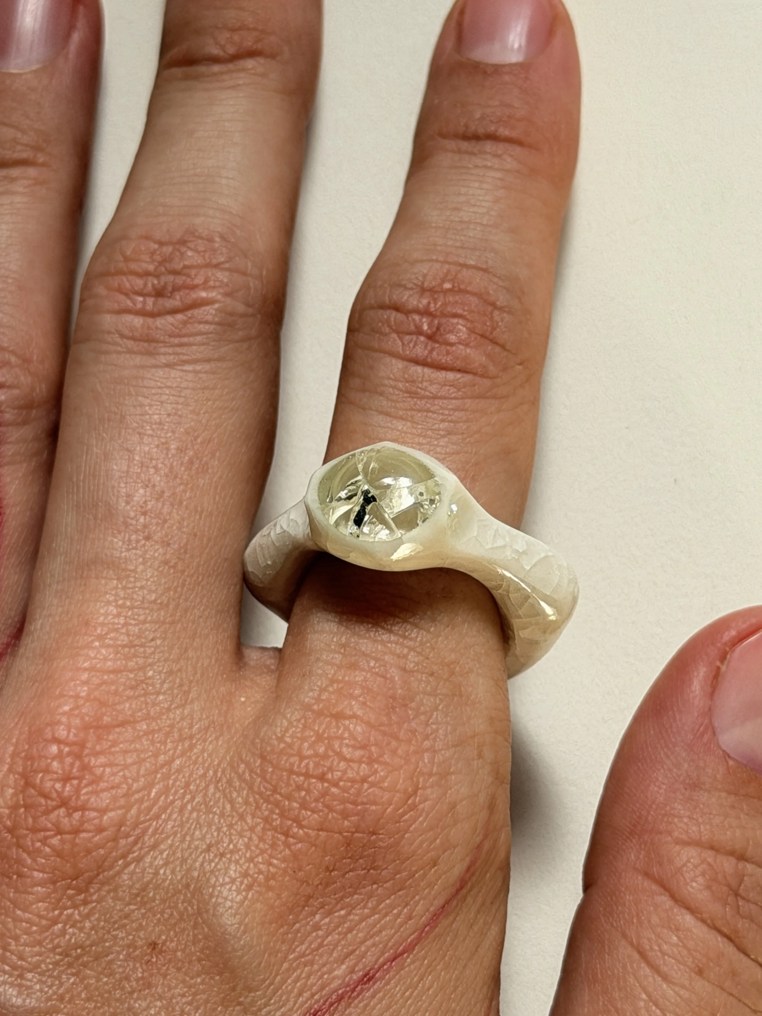 Close-up of Bone-white porcelain ring with crackle surface worn on hand, glass jewel visible