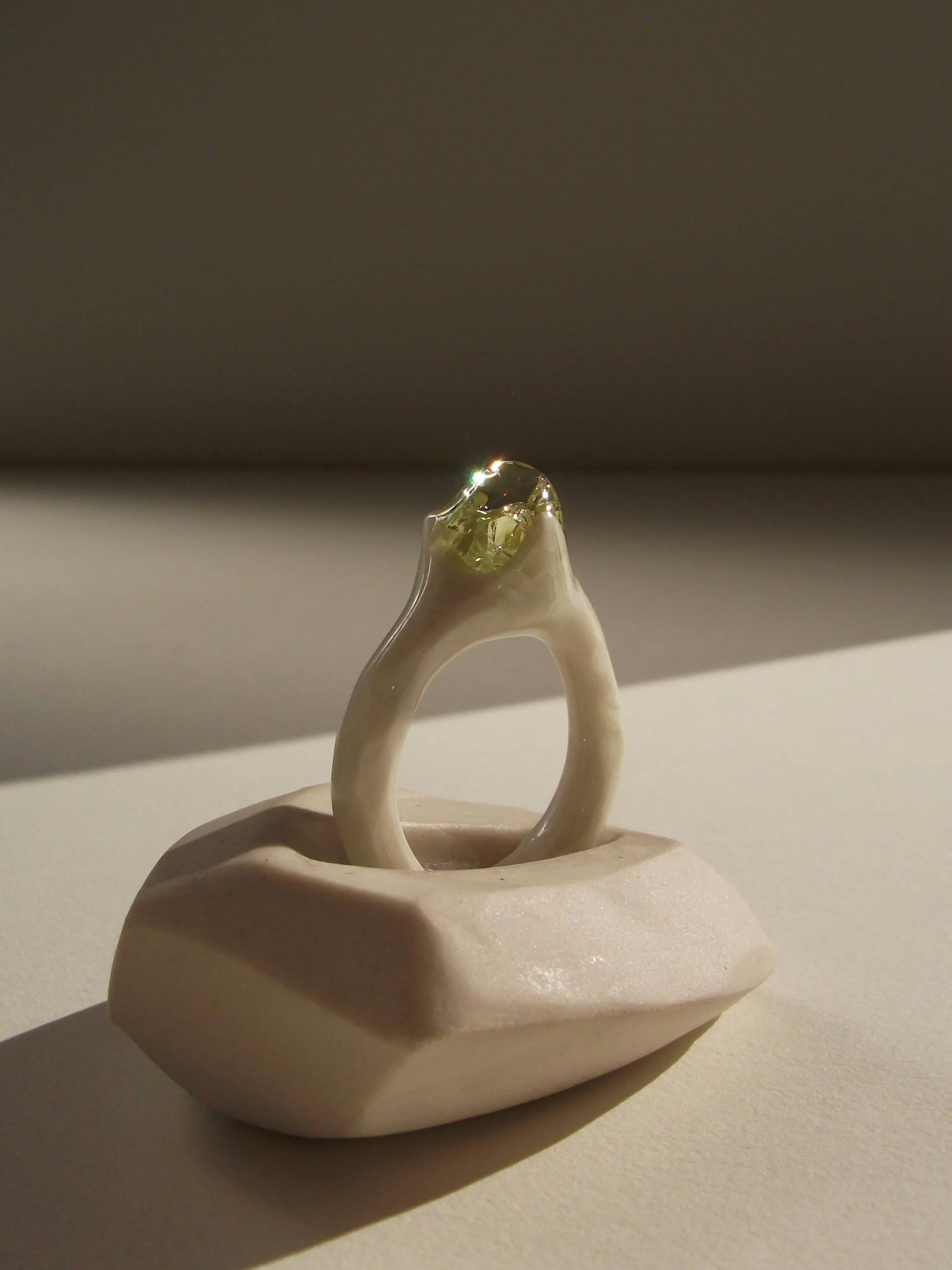 Angled view of bone-white porcelain ring with thin band and glass droplet