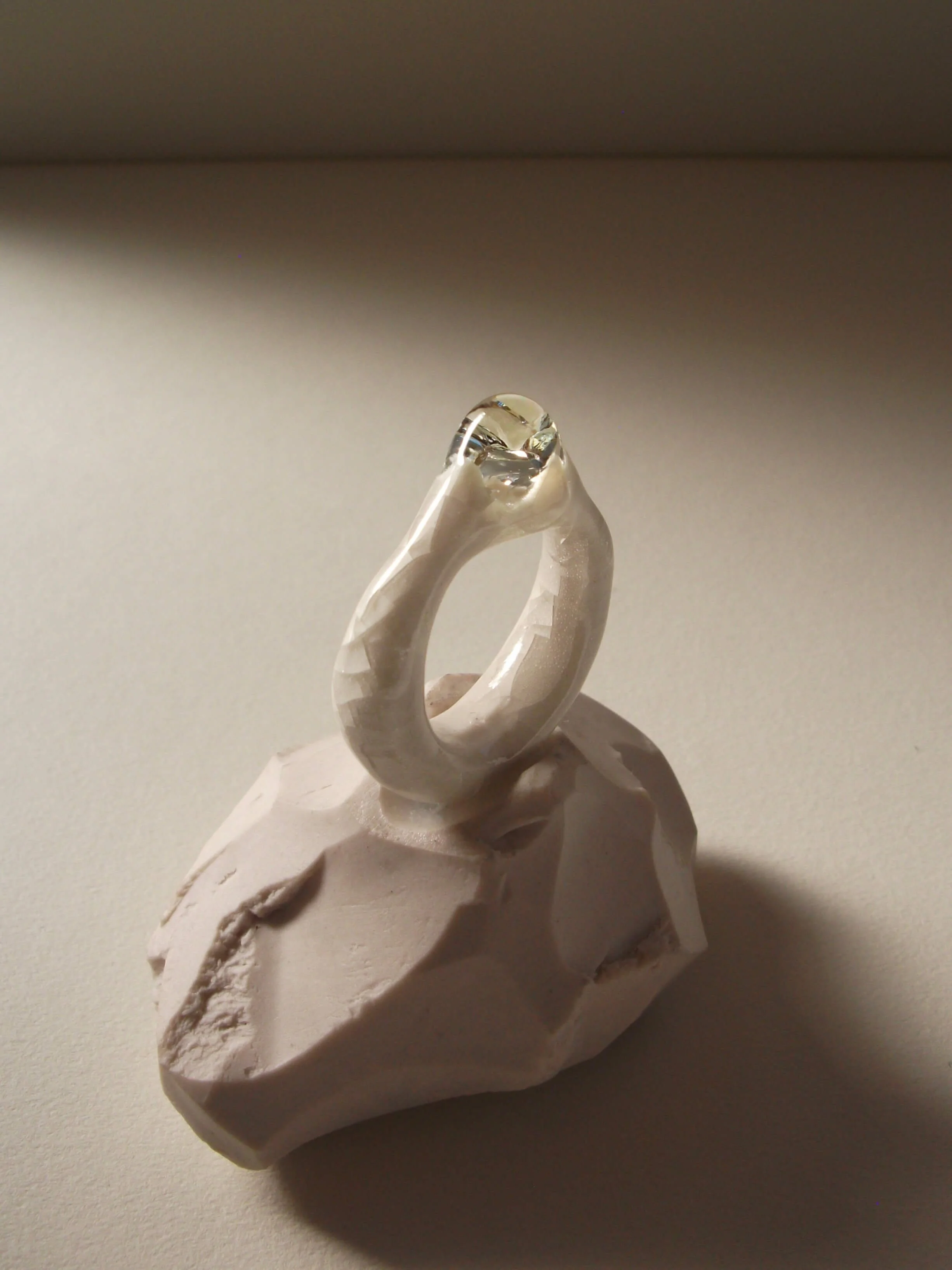 Side view of bone-white porcelain ring with medium-wide band, crackle surface, and large glass droplet